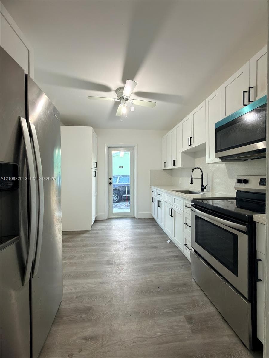 Kitchen featuring white cabinetry with matte black hardware, stainless steel appliances, wood-finish flooring, a matte black kitchen faucet, and a ceiling-mounted light fixture