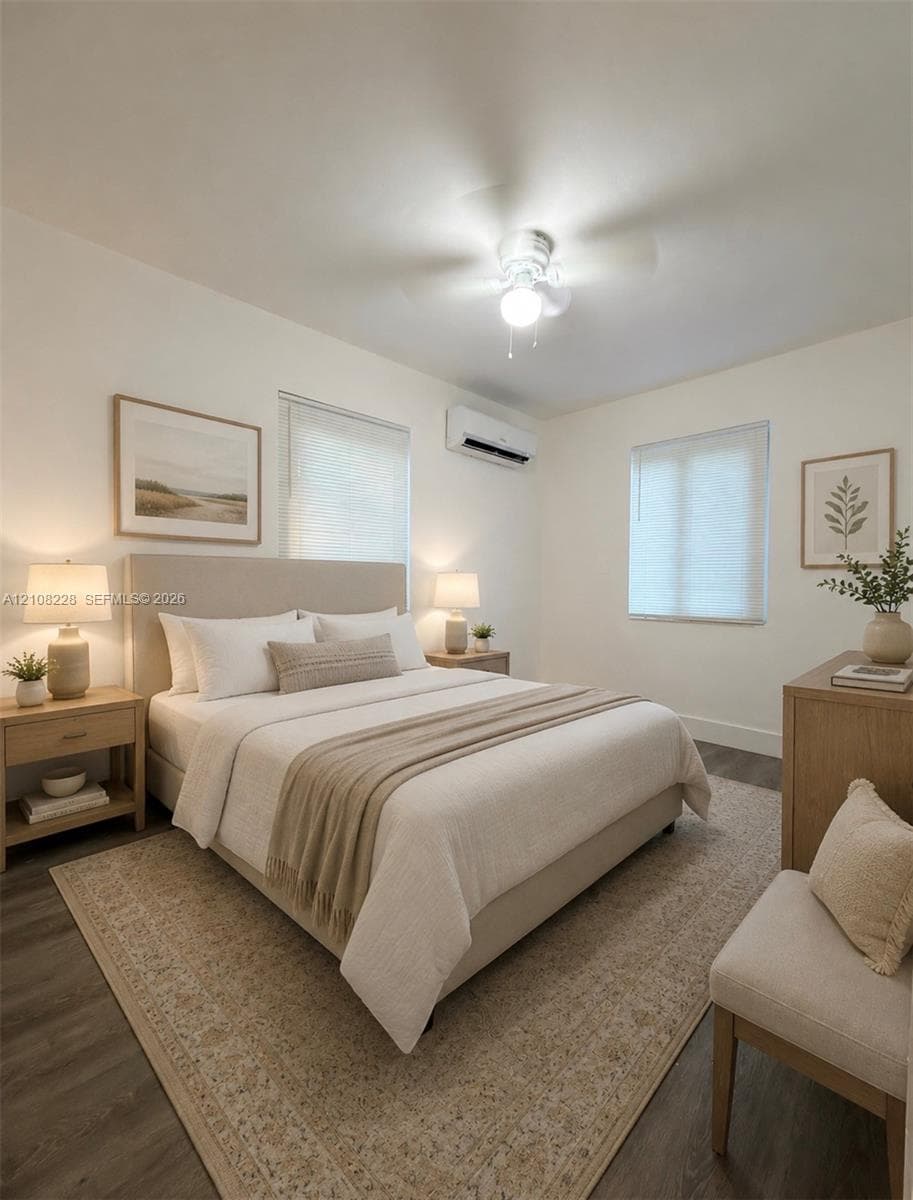Room featuring wood-finish flooring, a wall-mounted ductless air conditioning unit, neutral wall paint, two dual-pane windows with integrated blinds, and a ceiling-mounted light fixture with fan