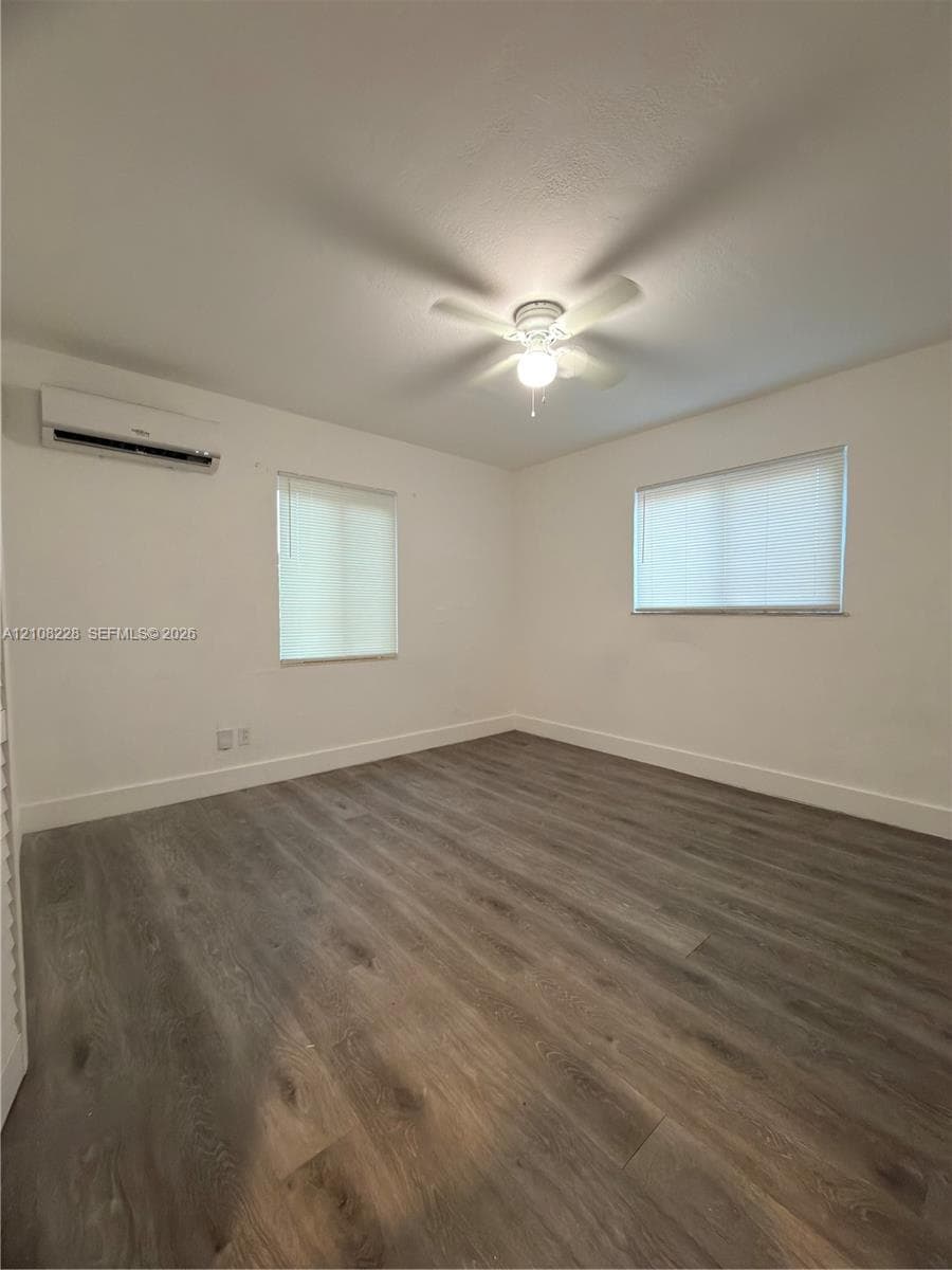 Room featuring wood-finish flooring, a wall-mounted ductless air conditioning unit, neutral walls, and a ceiling fan with integrated lighting