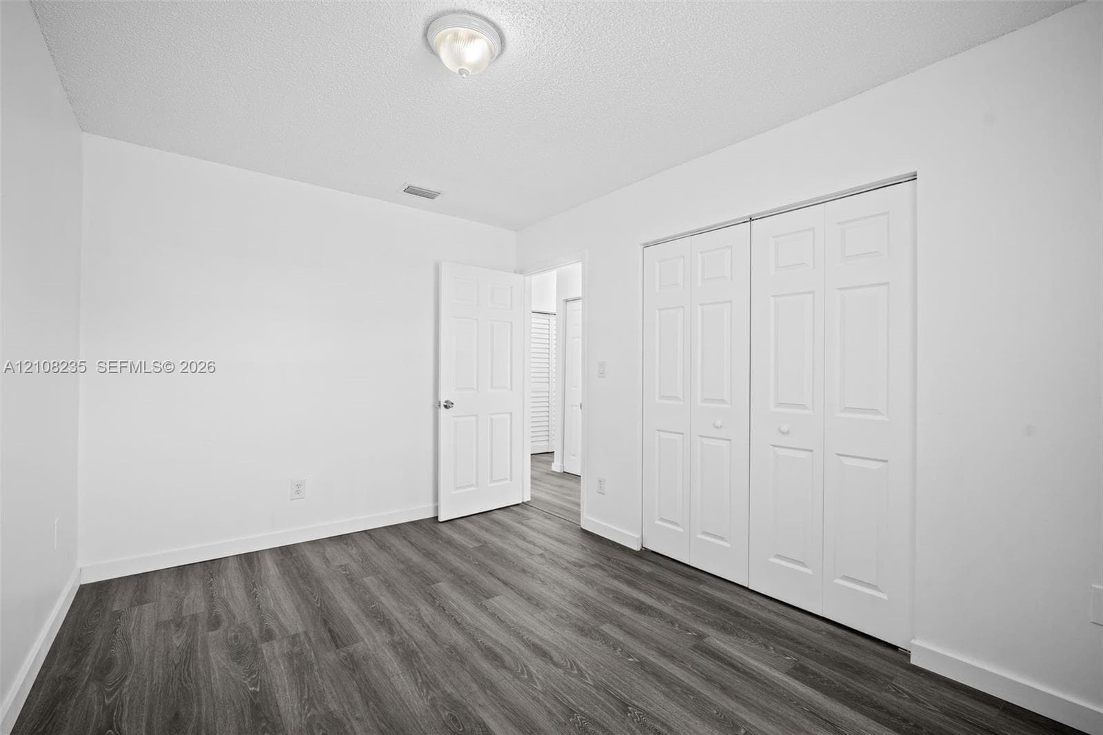 Neutral room featuring wood-finish flooring, double-panel closet doors, and a ceiling-mounted light fixture