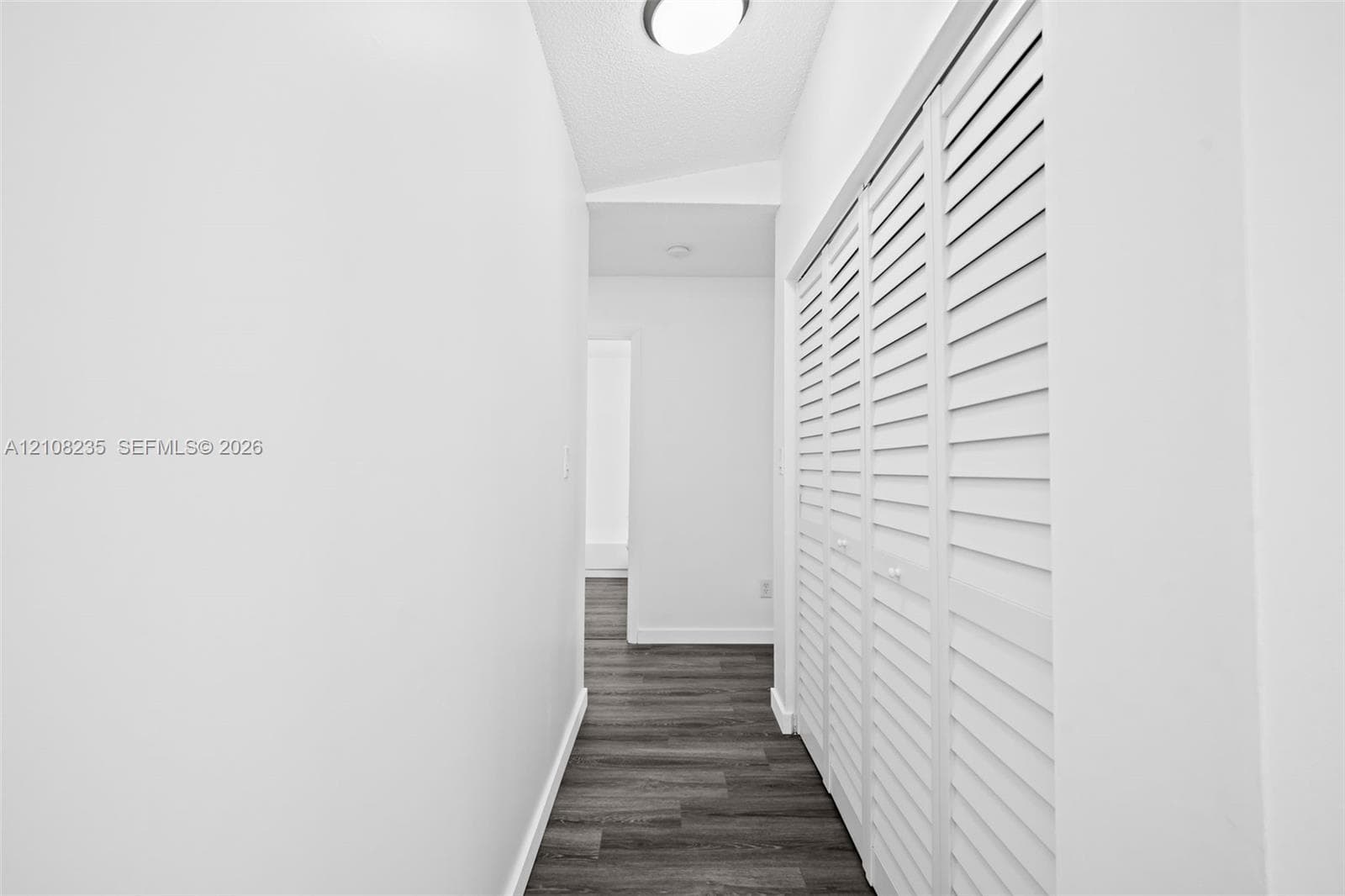 Hallway featuring wood-finish flooring and floor-to-ceiling white louvered bifold closet doors