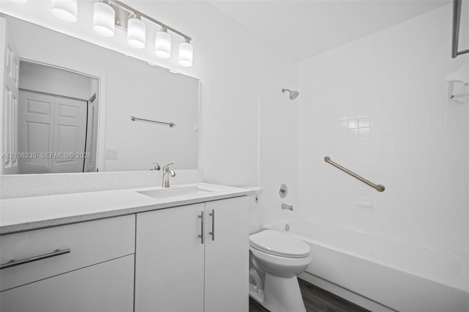 Bathroom featuring a white vanity with a solid surface countertop, an integrated sink, a full-width mirror, five-light overhead fixture, and a tile-surround shower and tub combination