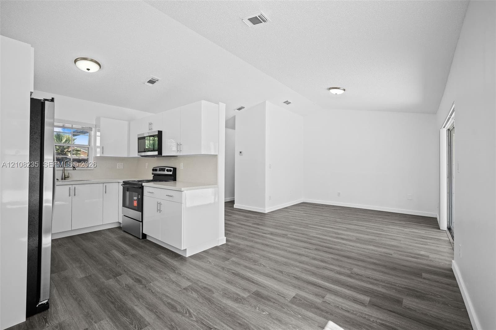 Kitchen featuring white cabinetry, solid-surface countertops, stainless steel appliances, and wood-finish flooring