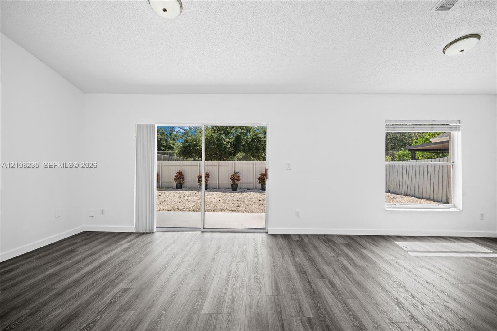 Interior space featuring wood-finish flooring, vaulted ceilings, dual flush-mount light fixtures, and a sliding glass door providing access to the rear exterior