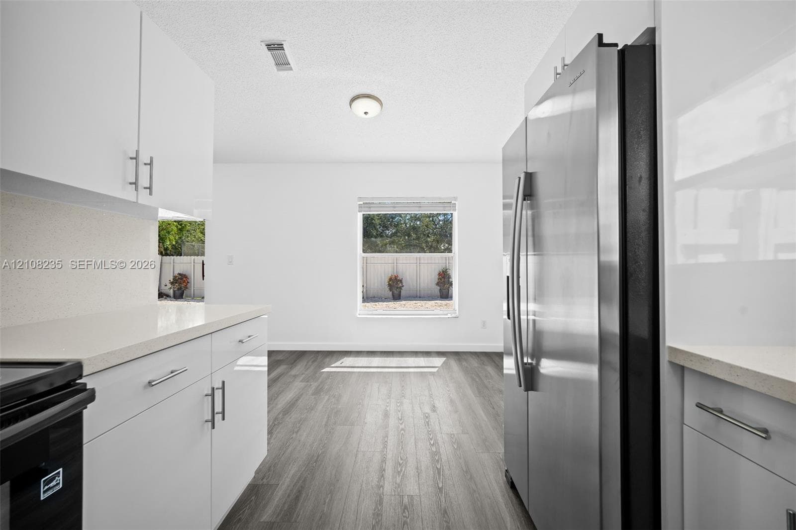 Kitchen featuring white flat-panel cabinetry, light-toned stone-surface countertops, wood-finish flooring, and a stainless steel side-by-side refrigerator