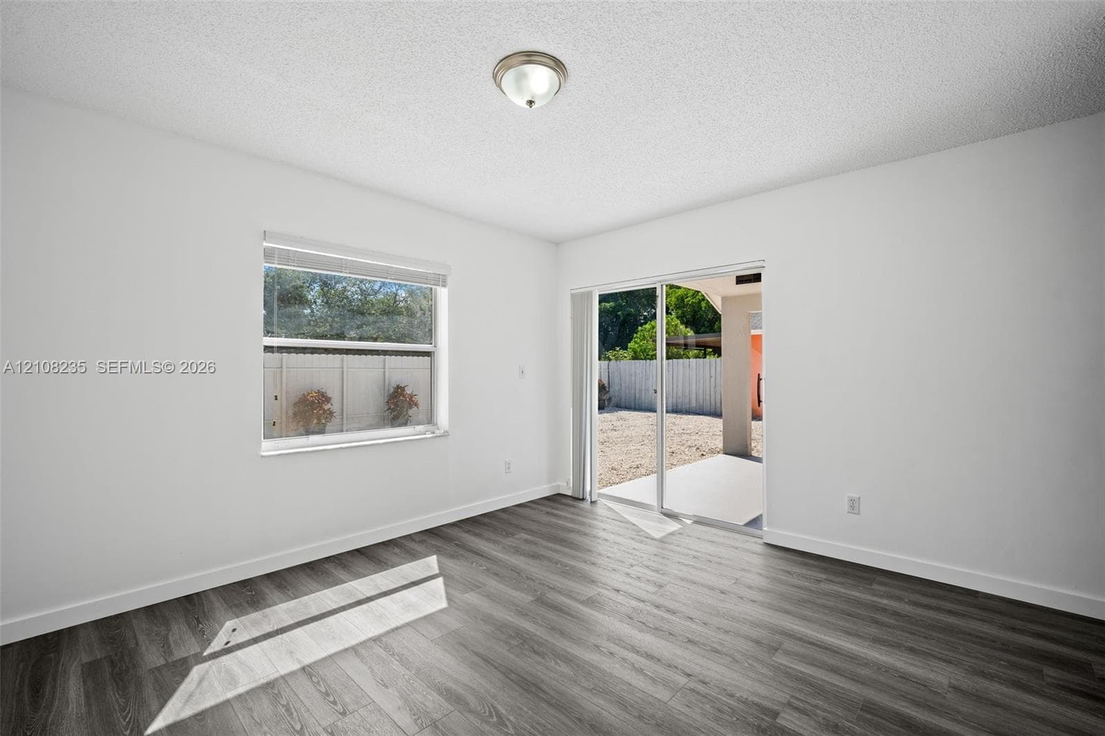 Interior space featuring wood-finish flooring, sliding glass door, single-pane window, and a central ceiling-mounted light fixture