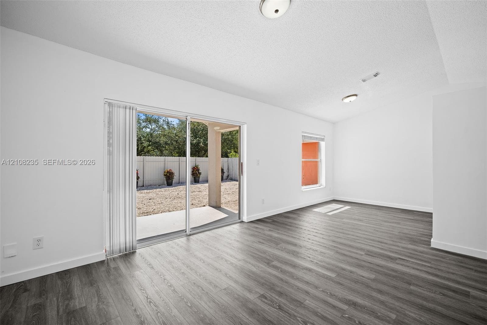Interior space featuring wood-finish flooring, white walls, flush-mount ceiling lighting, a single-pane window, and glass sliding doors providing access to a covered concrete patio