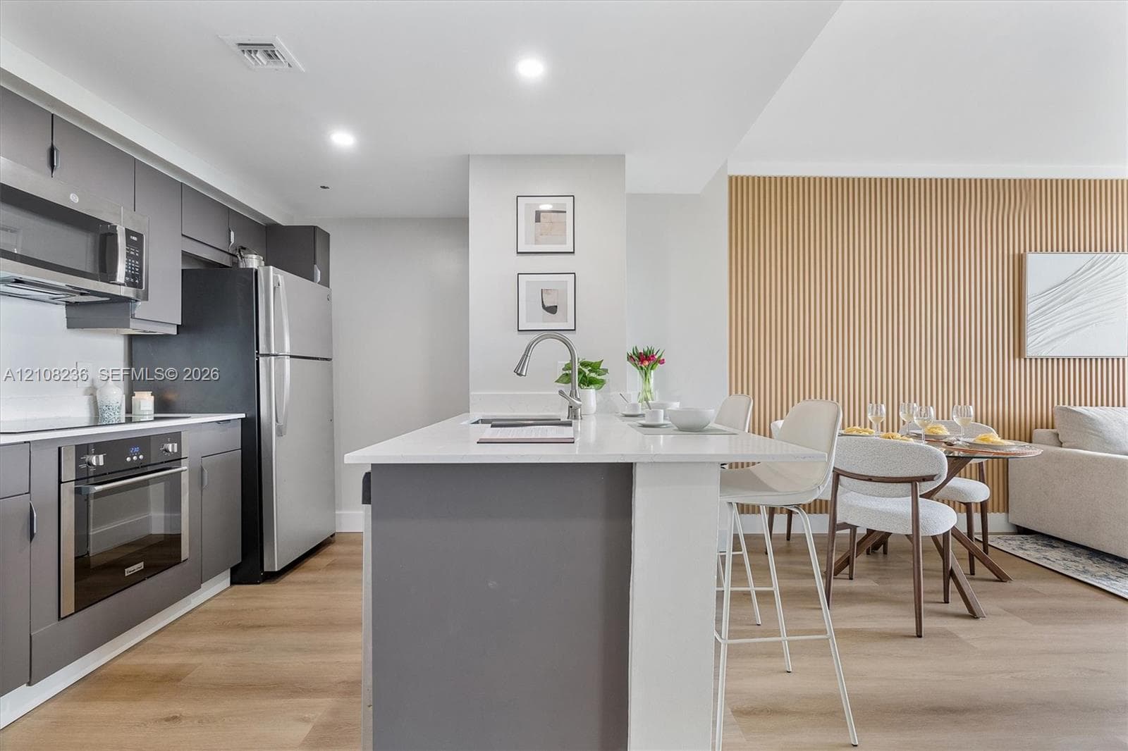 Kitchen featuring a central island with a solid-surface countertop, stainless steel appliances, flat-panel grey cabinetry, wood-finish flooring, and a decorative vertical wood-slat accent wall