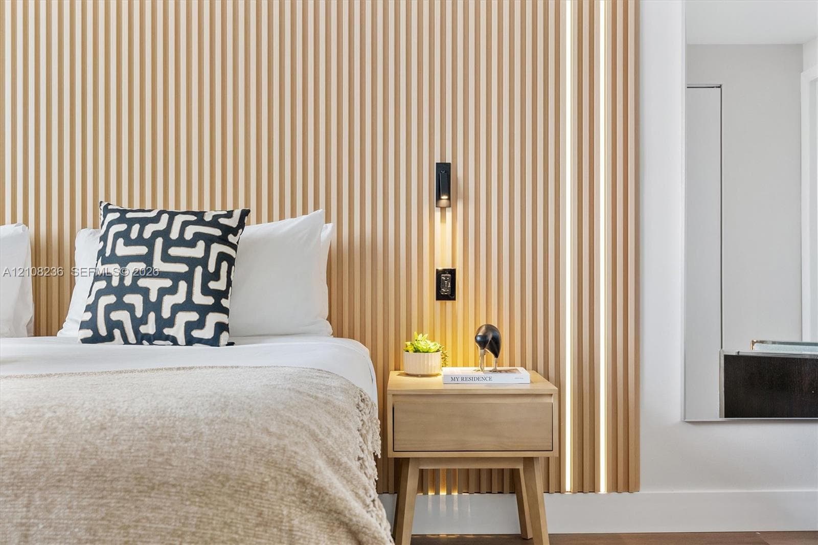 Floor-to-ceiling slatted wood wall paneling with integrated vertical LED accent lighting and a matte black wall-mounted reading light