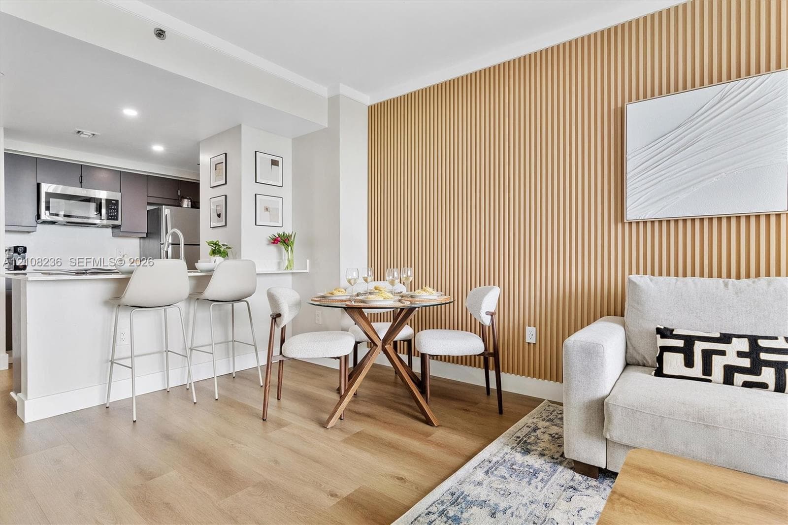 Vertical slat wood-finish accent wall, wood-finish flooring, and kitchen featuring dark cabinetry, stainless steel appliances, and a quartz countertop breakfast bar