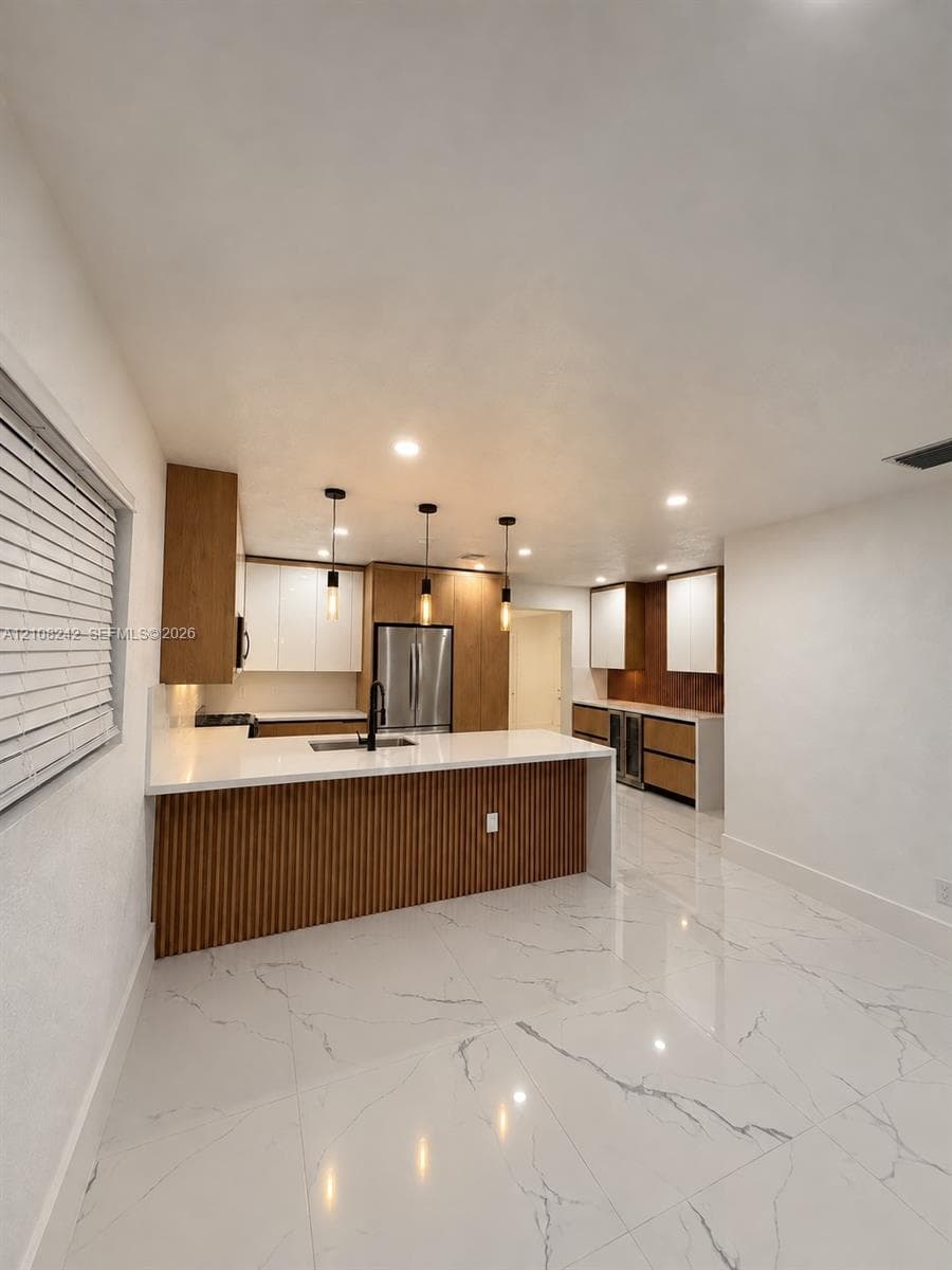 Kitchen featuring custom two-tone cabinetry with slatted wood detailing, white stone countertops, large-format veined porcelain tile flooring, stainless steel built-in appliances, and pendant lighting