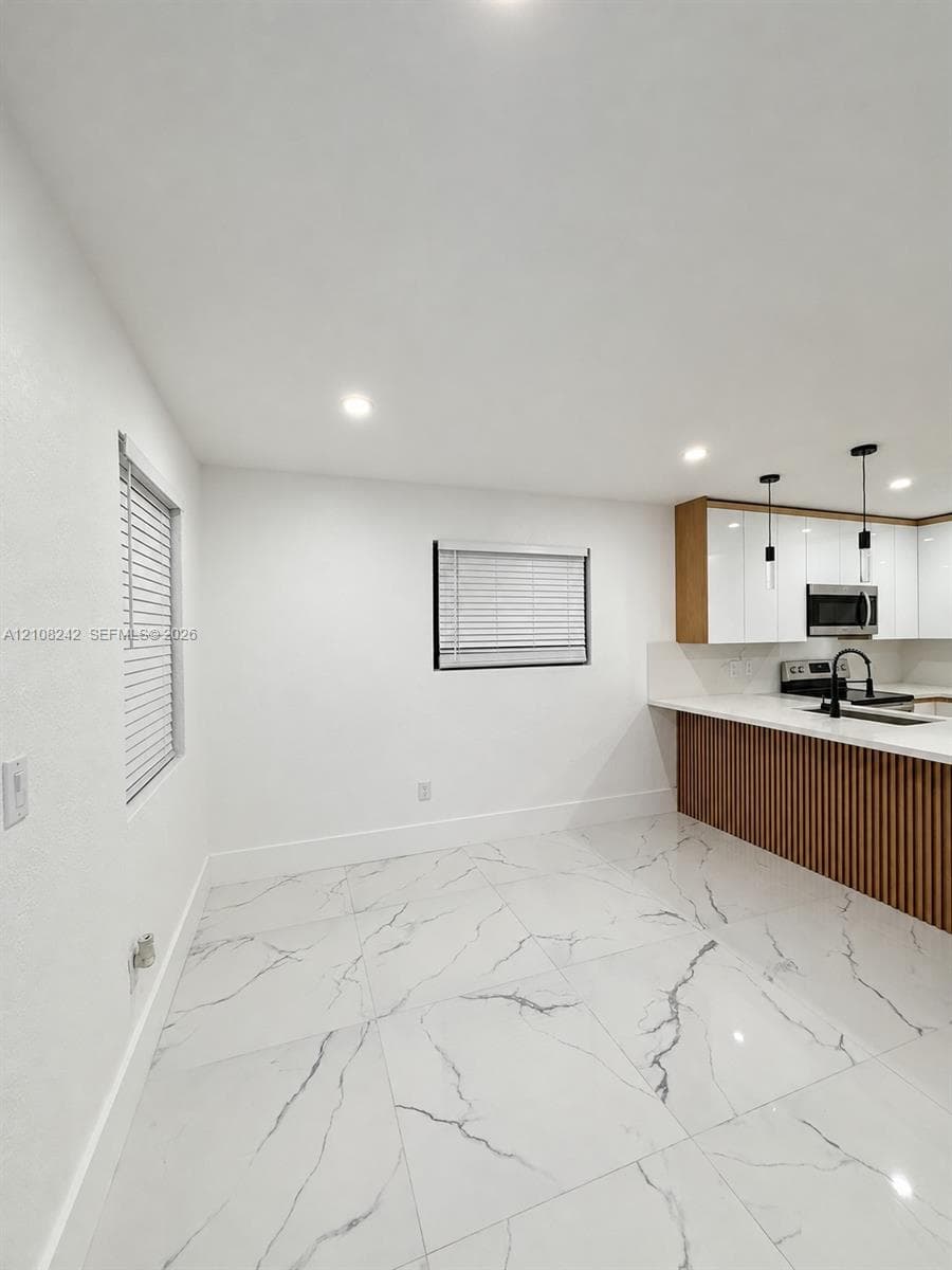 Large-format tile flooring, white gloss cabinetry, vertical wood-slat kitchen island detailing, matte black fixtures, and recessed ceiling lighting