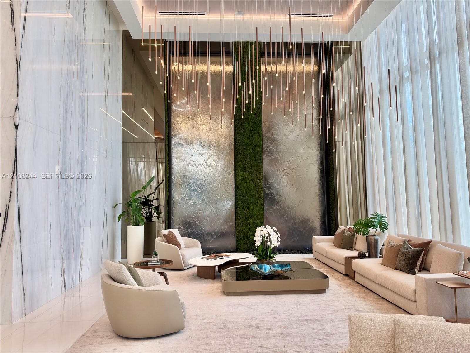 Double-height ceiling, large-scale veined stone wall cladding, floor-to-ceiling windows, custom tiered pendant lighting, and a floor-to-ceiling illuminated water feature with a central vertical moss panel