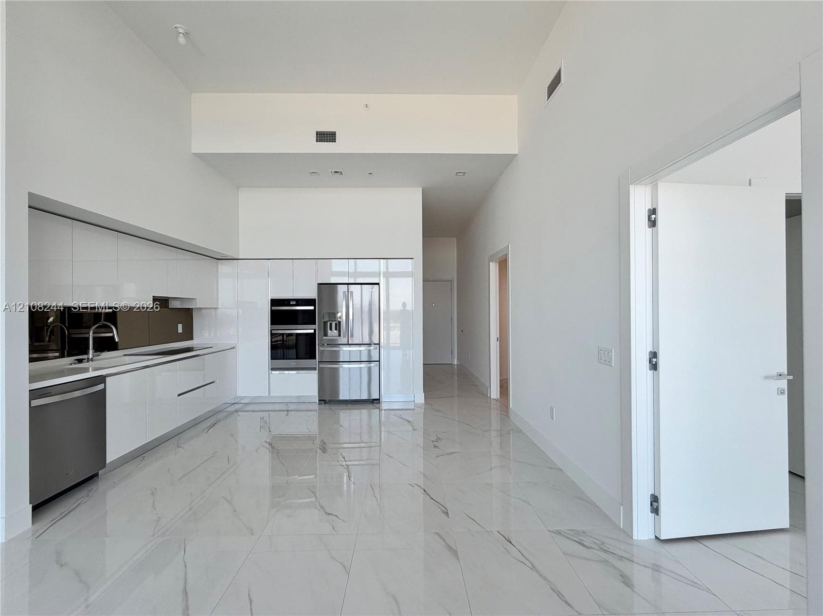 High-gloss cabinetry, stone-finish tile flooring, integrated stainless steel appliances, wall-mounted oven, and high ceilings