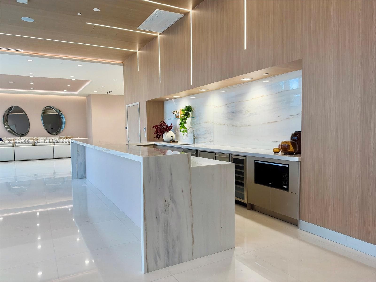Custom kitchen area featuring stone slab countertops, waterfall-edge island, integrated cabinetry, light-toned wood paneling, and vertical recessed lighting