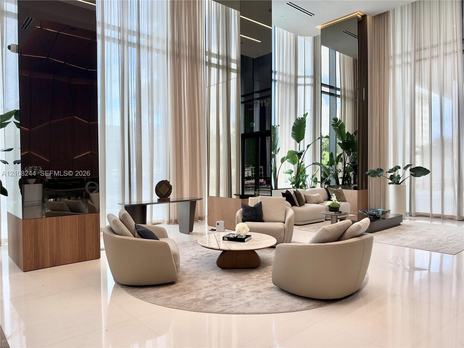 Double-height ceilings featuring floor-to-ceiling glass windows, polished stone flooring, and mirrored architectural columns