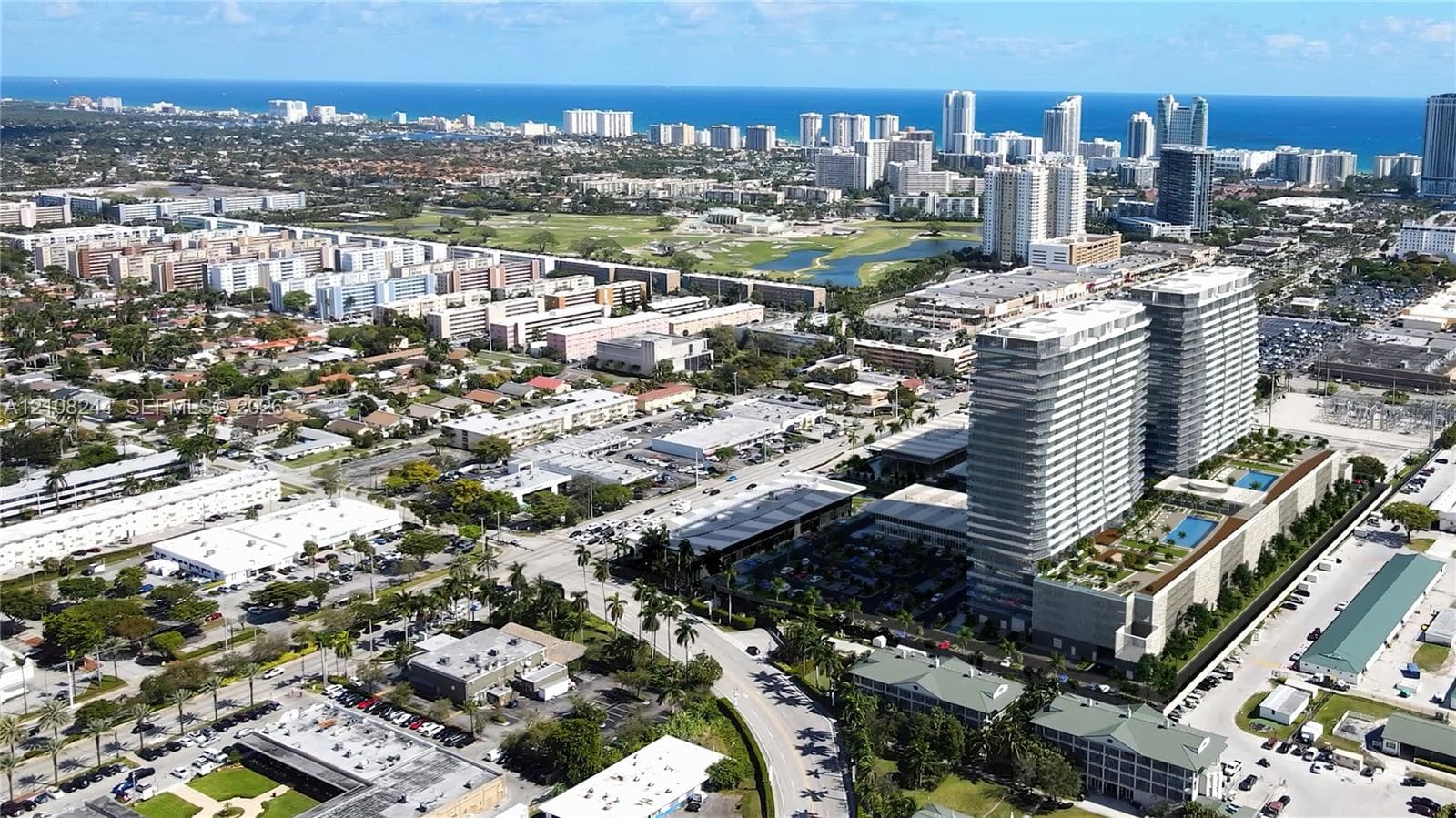 Aerial perspective of high-rise residential towers featuring podium-level swimming pools, landscaped outdoor recreation areas, and proximity to the coastline
