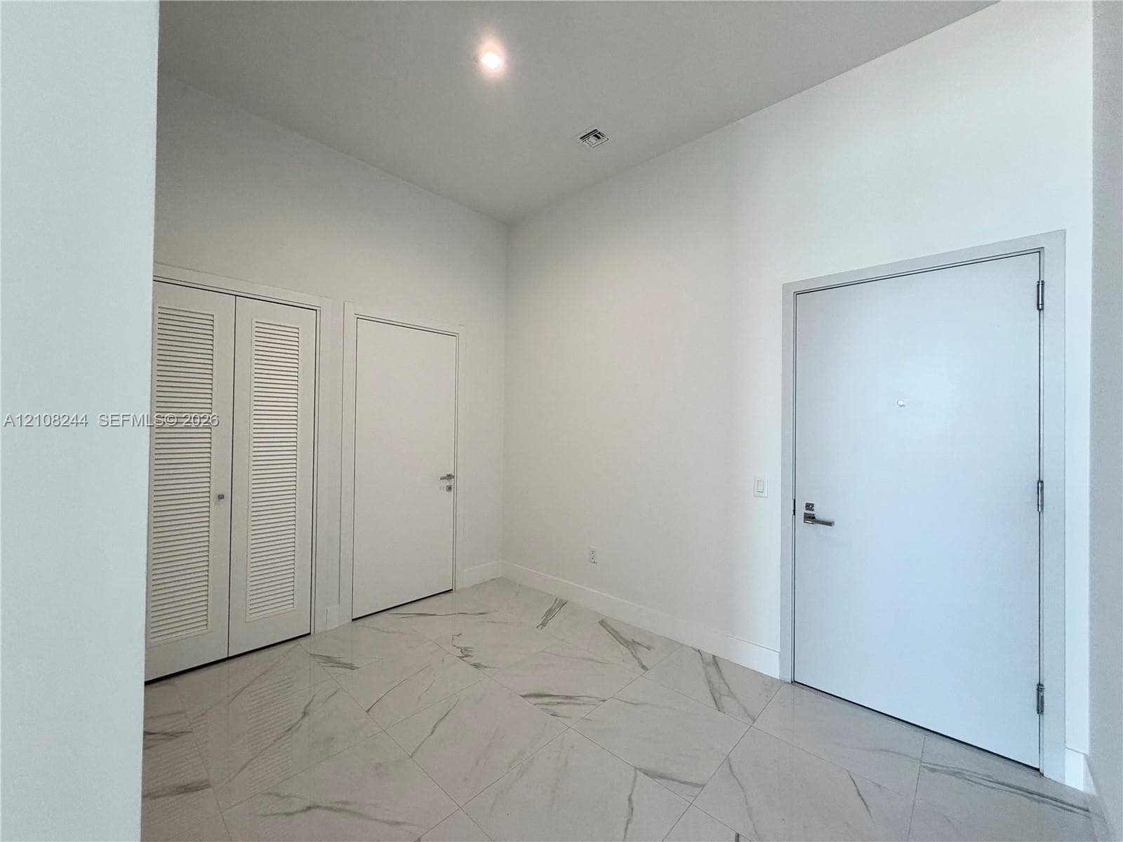 High-ceiling interior featuring stone-finish tile flooring with veining detail, recessed lighting, and white louvered-panel closet doors
