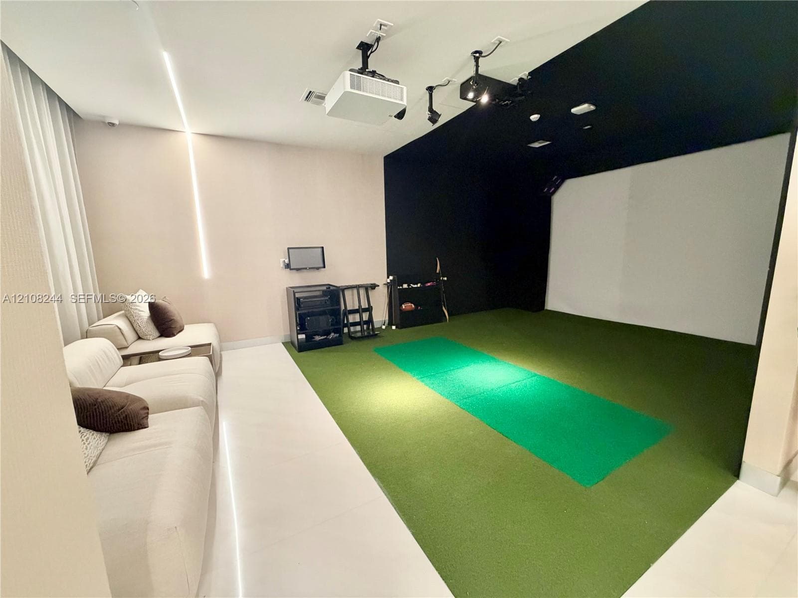 Recreation room featuring integrated projector equipment, a specialized synthetic turf flooring area, high-contrast ceiling paint, and minimalist vertical accent lighting