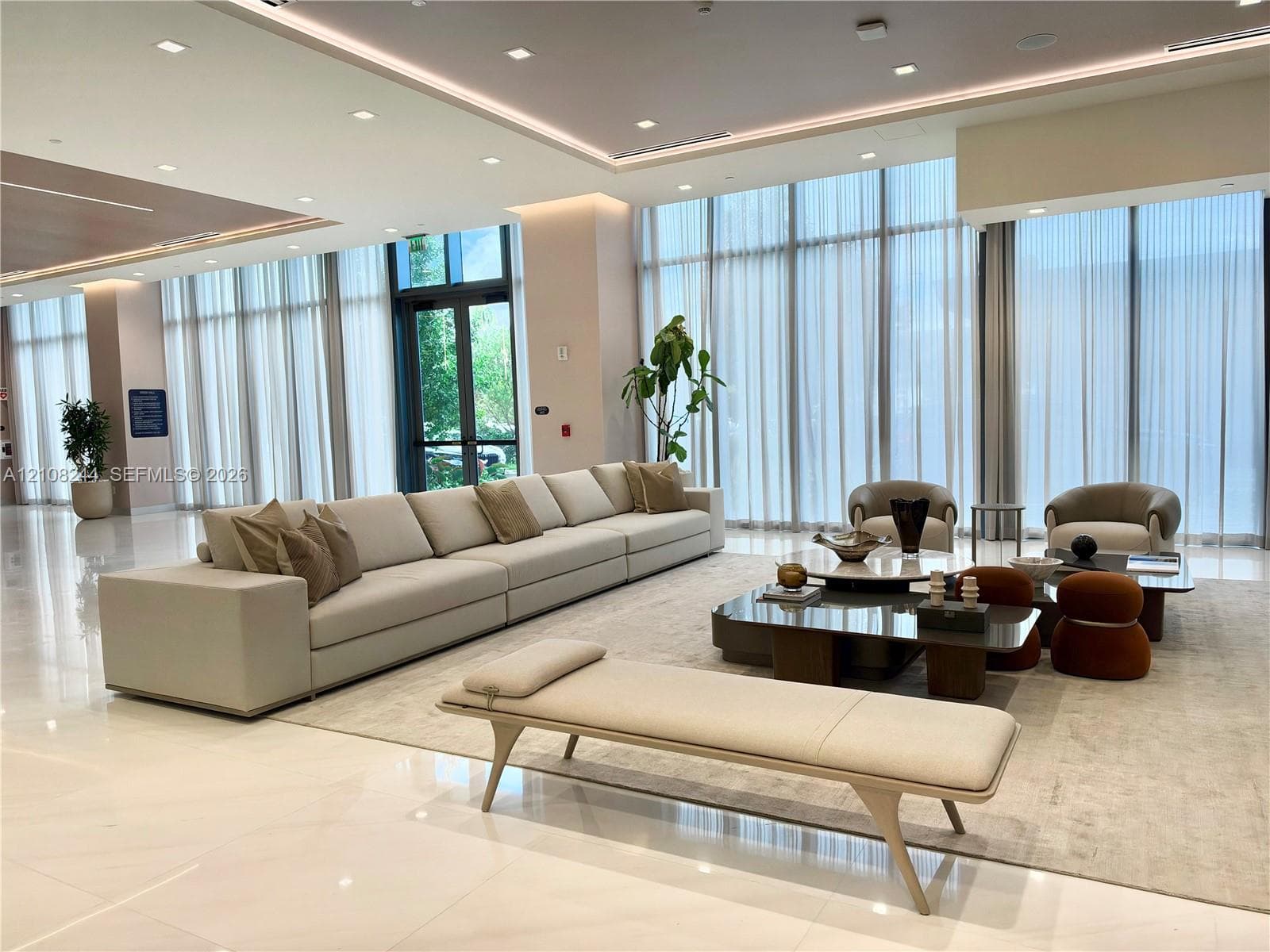Expansive common area featuring floor-to-ceiling windows, polished stone tile flooring, recessed ceiling lighting, and layered tray ceiling detail