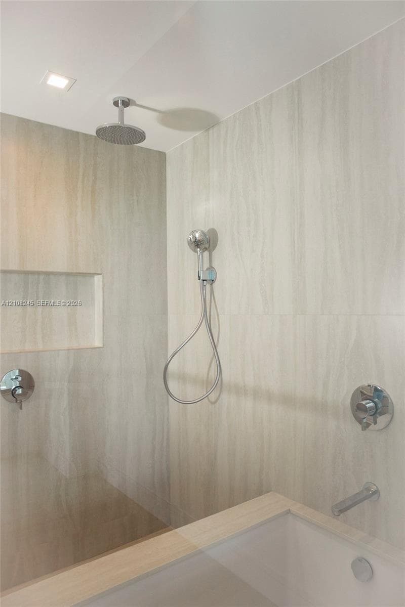 Walk-in shower featuring large-format tile surround, recessed wall niche, chrome rainfall shower head, handheld sprayer, and polished chrome hardware