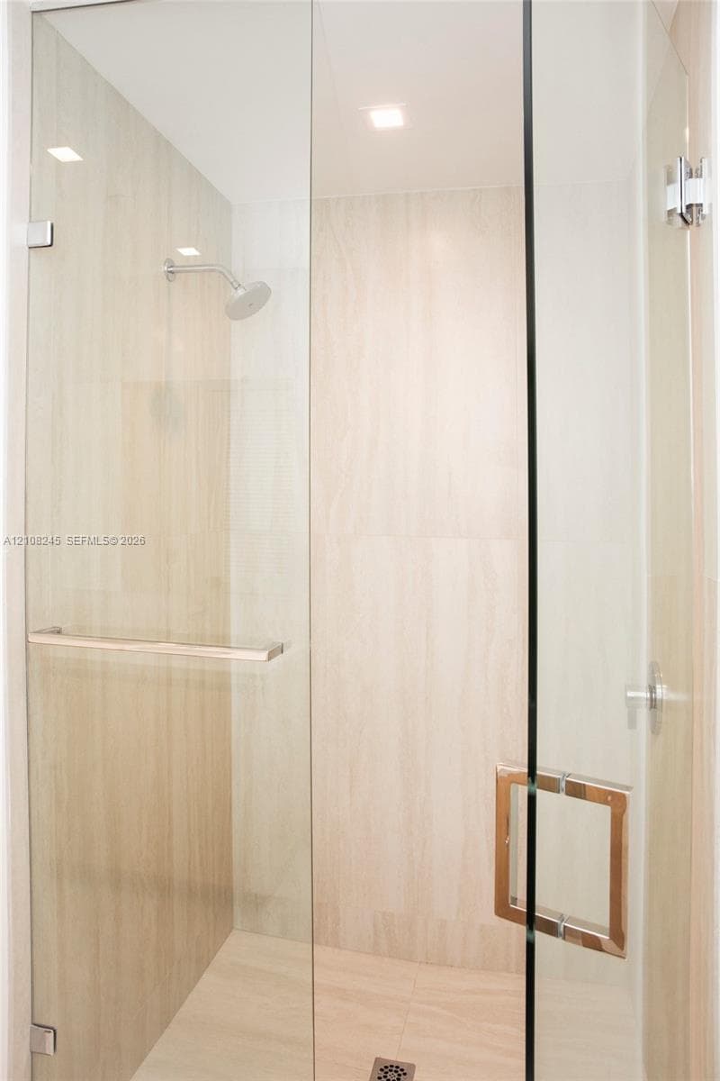 Walk-in shower enclosure featuring floor-to-ceiling neutral stone-finish tile, frameless glass paneling, polished chrome hardware, and an integrated wall-mounted showerhead
