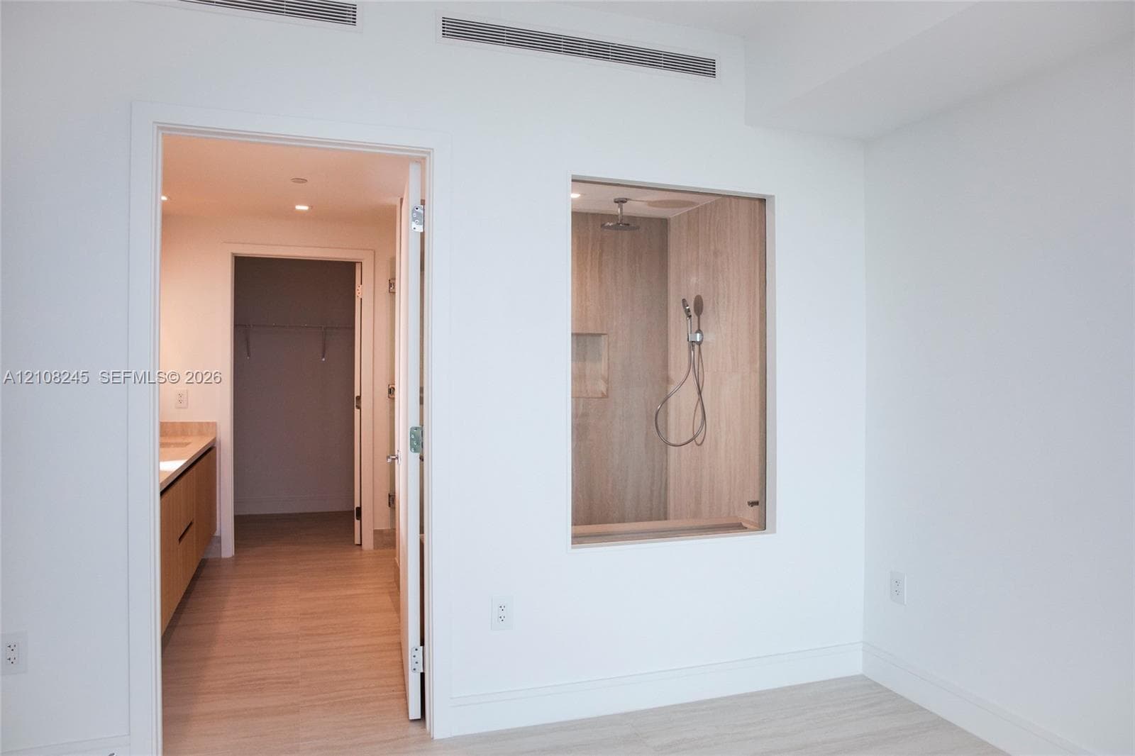 Shower enclosure with a glass partition, wall-mounted shower head, and built-in wall niche, featuring wood-finish wall tile and wood-finish flooring