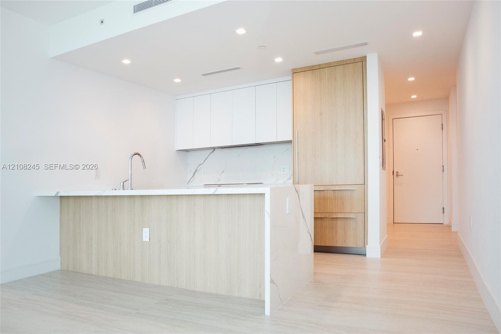 Kitchen featuring wood-finish cabinetry, white matte upper cabinets, stone-surfaced island with waterfall edge, integrated refrigerator, and recessed lighting