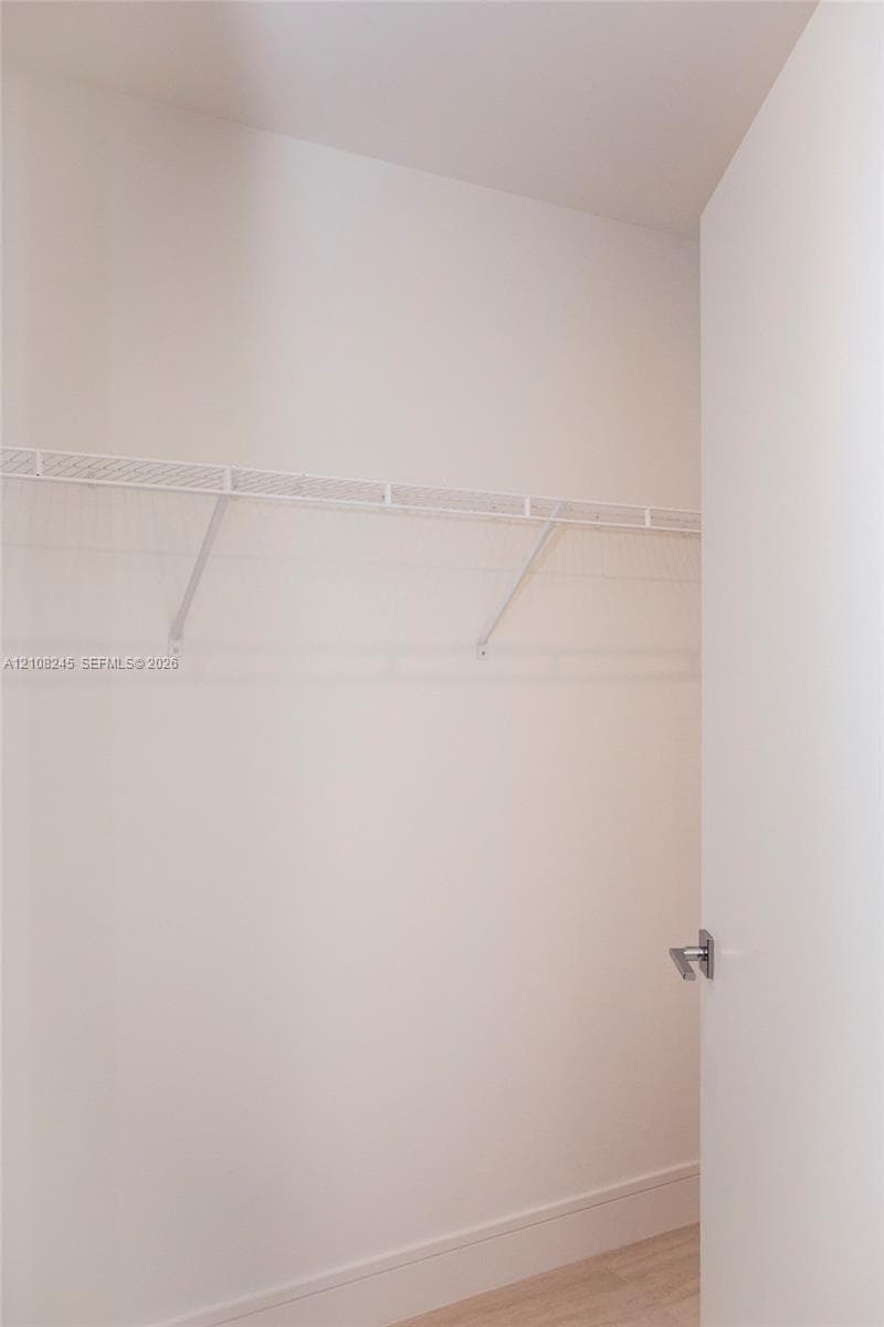 Storage space featuring a white wire shelving system, a mounted garment rod, and neutral flooring