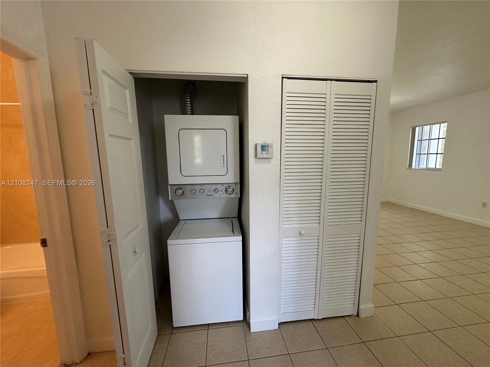 Laundry closet featuring a stackable washer and dryer unit, louvered bi-fold doors, and tile flooring
