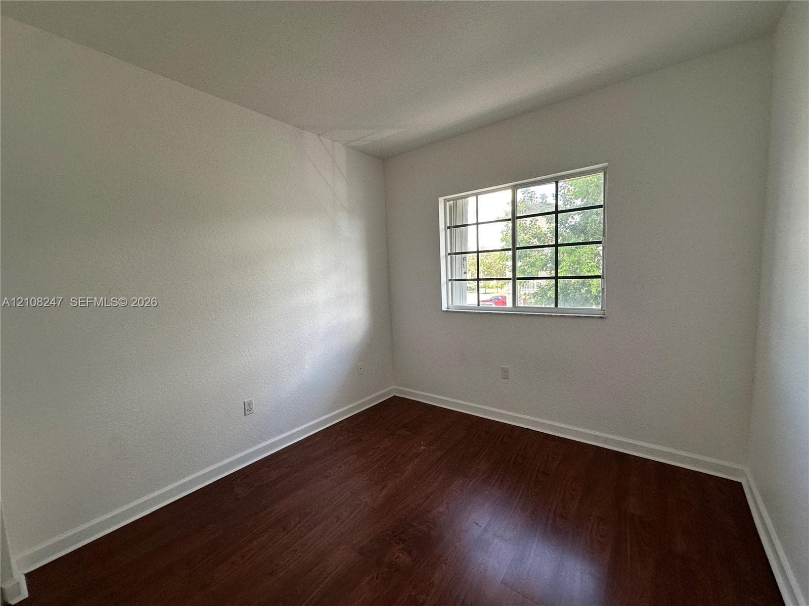 Room featuring wood-finish flooring, white walls, and a multi-pane sliding window