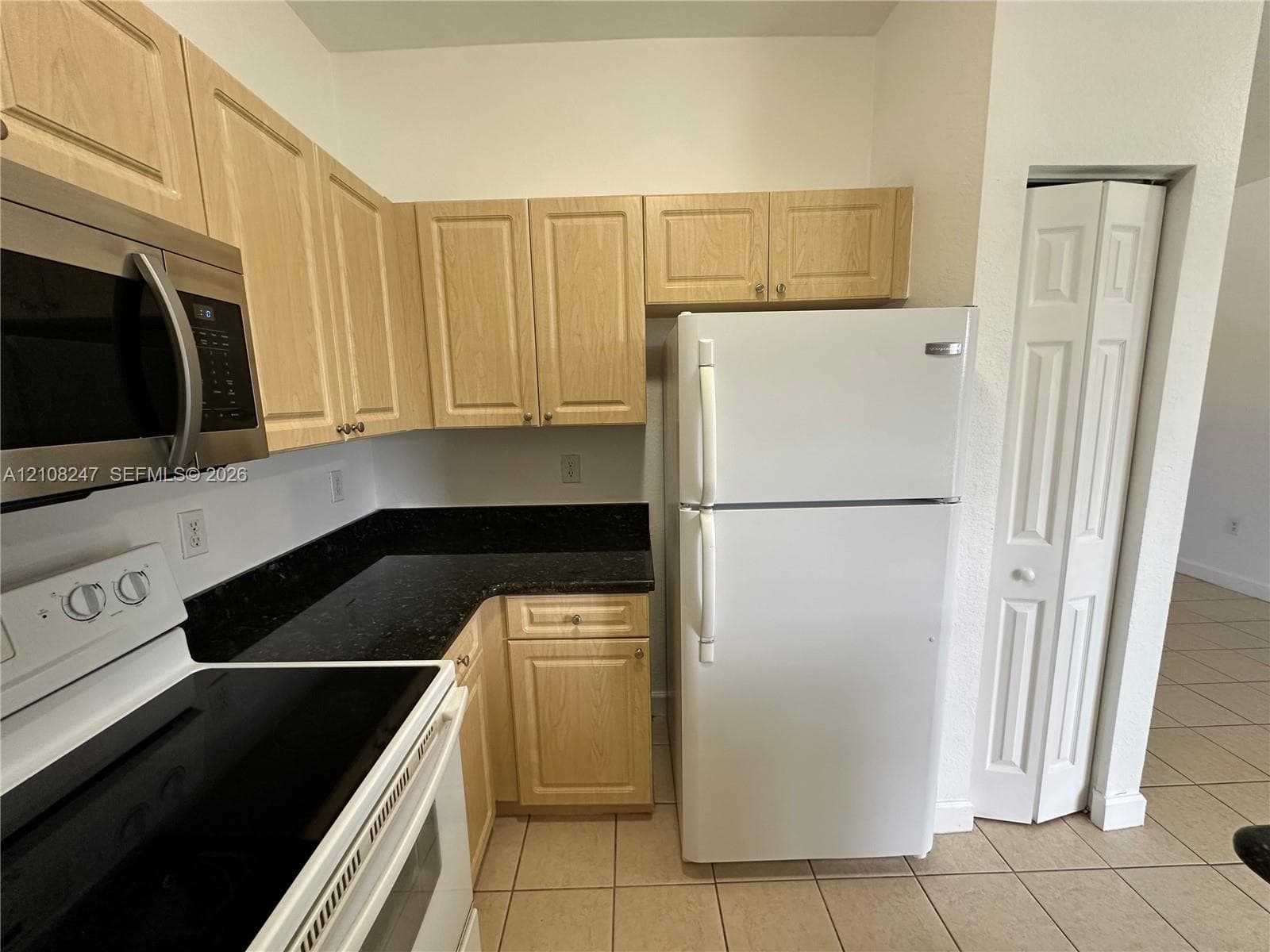 Kitchen featuring light-finish cabinetry, dark stone-style countertops, white appliance suite, and ceramic tile flooring
