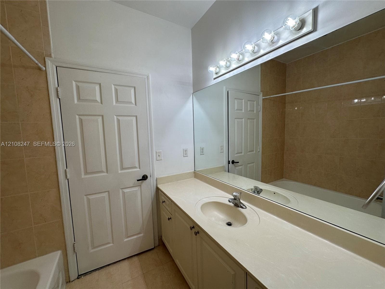 Full-width wall mirror, vanity cabinet with integrated countertop and sink, six-bulb light fixture, and floor-to-ceiling tiled shower enclosure