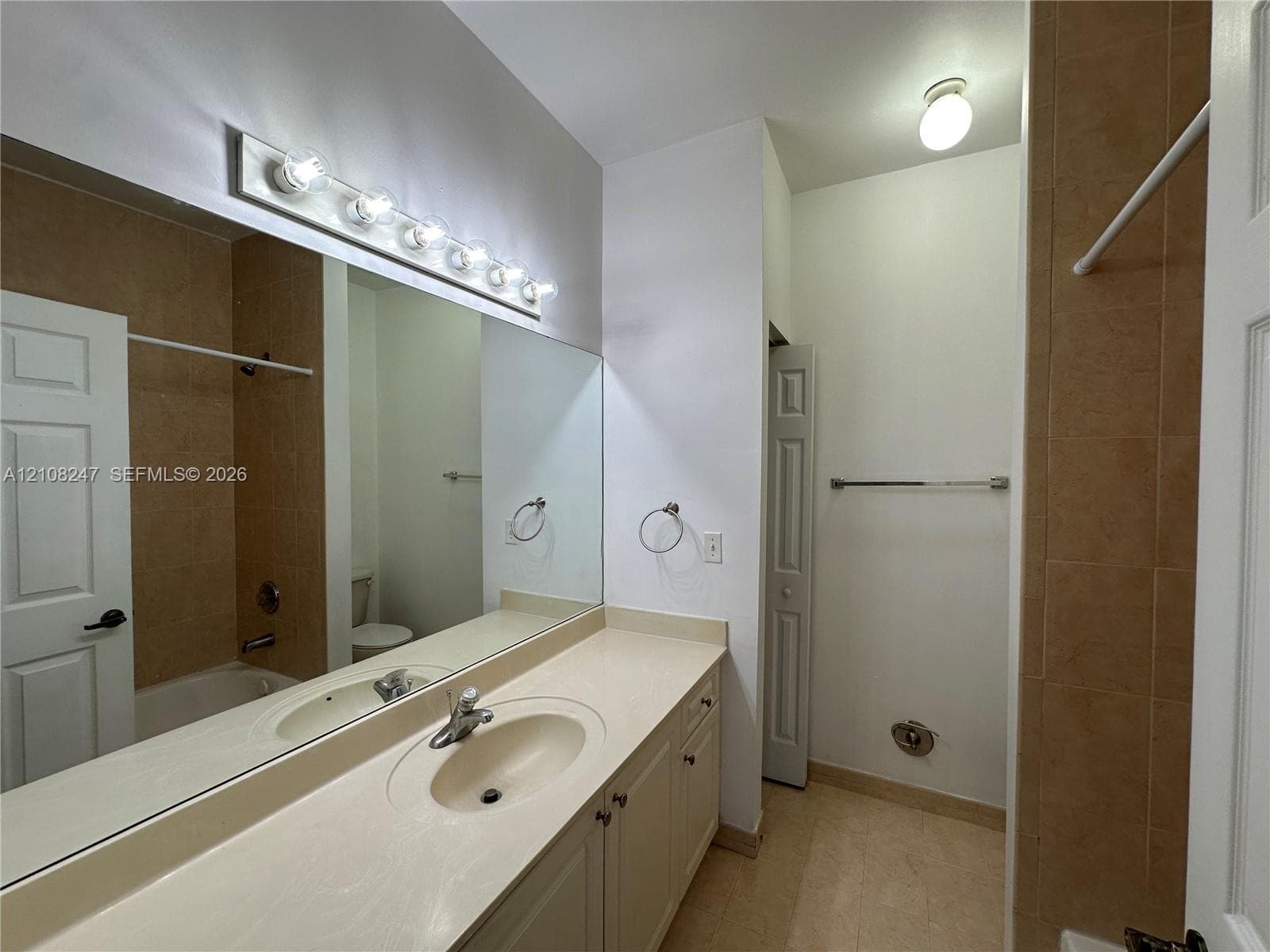 Bathroom featuring a neutral vanity with an integrated sink, a full-width vanity mirror, a six-bulb wall-mounted light fixture, and tile-surround tub area