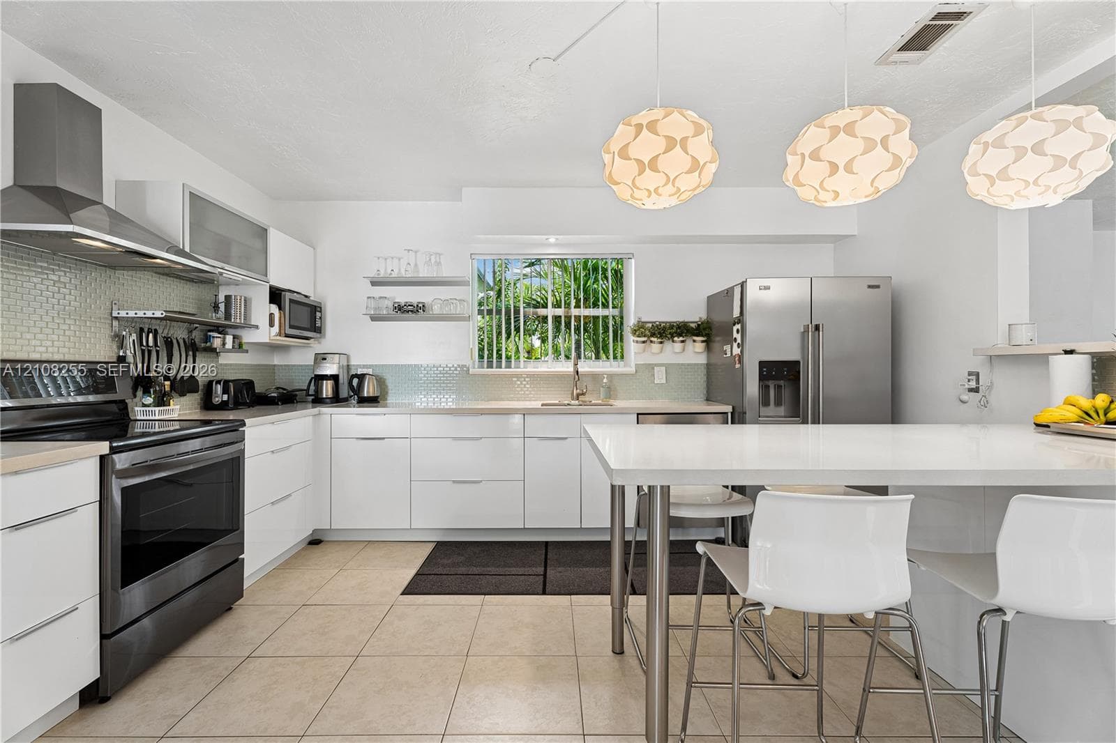 Kitchen featuring white flat-panel cabinetry, stainless steel appliances, a tile backsplash, and a central island with a solid-surface countertop