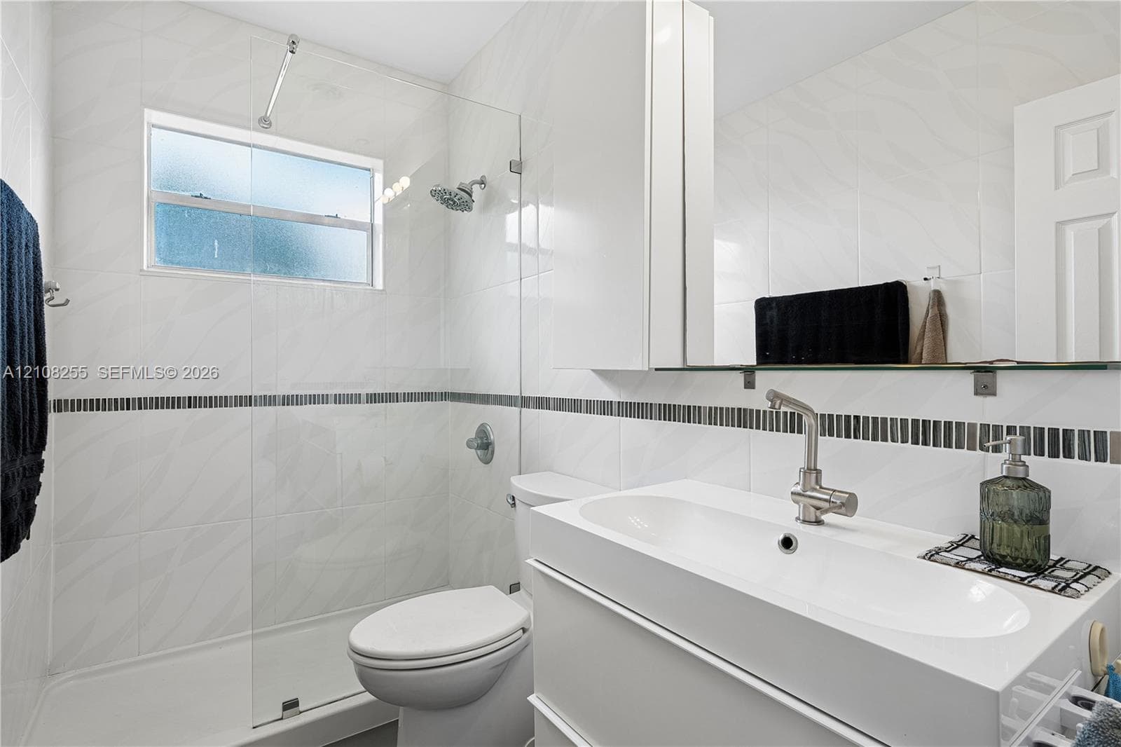 Bathroom featuring white wall tile with a mosaic accent border, a glass-enclosed shower, a floating vanity with an integrated sink, and brushed-nickel hardware