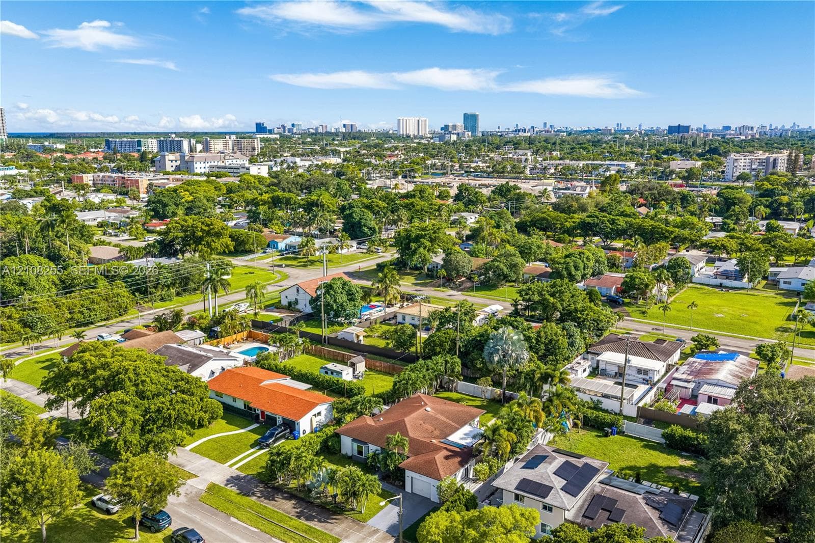 Aerial perspective of a suburban neighborhood featuring extensive mature tree canopy, residential lots with manicured lawns, and rooftops equipped with solar energy panels