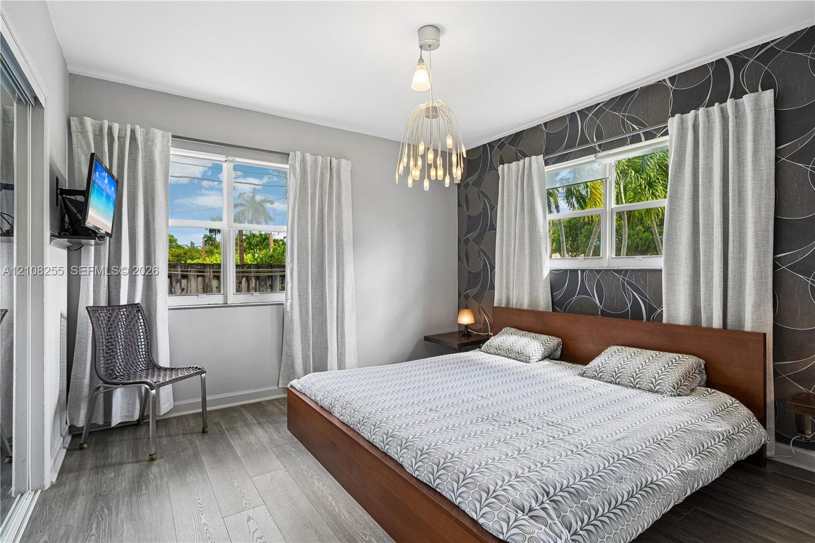 Wood-finish flooring, accent wall with patterned wall covering, multi-light pendant fixture, and large windows