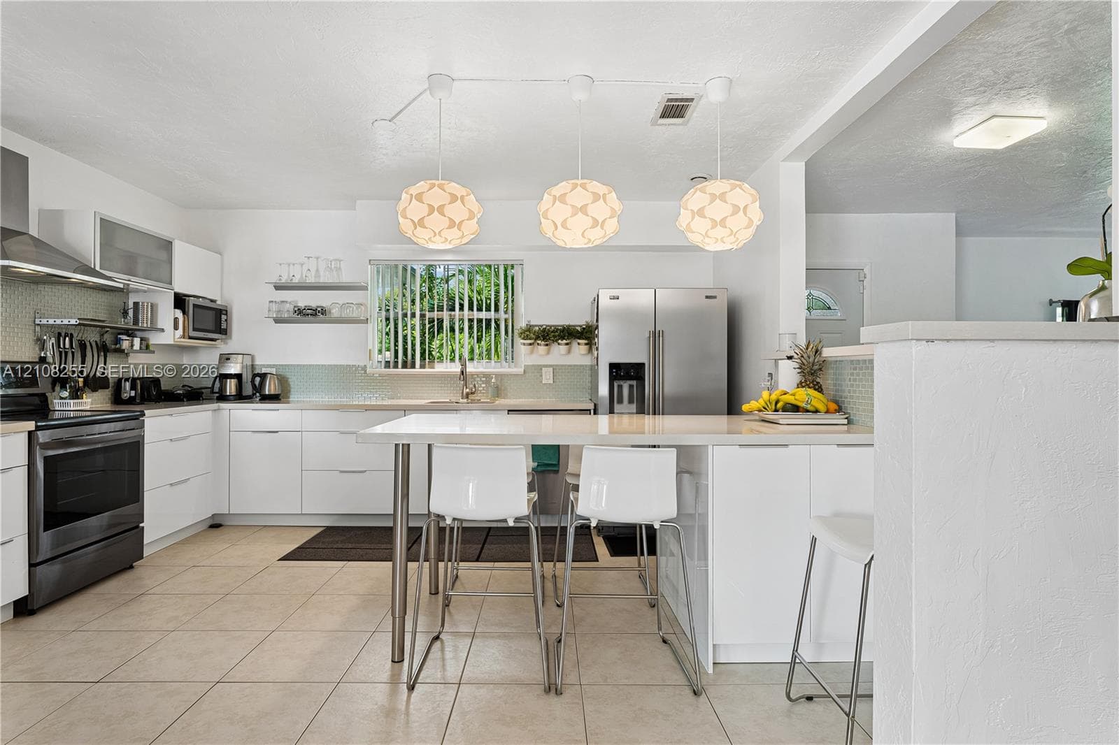 Kitchen featuring flat-panel white cabinetry, stainless steel appliances, quartz countertops, a tile backsplash, and three suspended geometric pendant lights