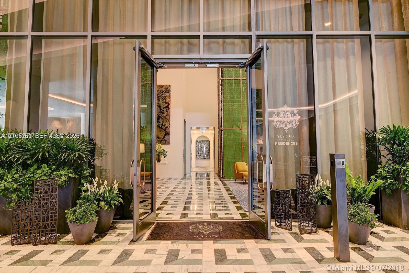Grand entrance featuring floor-to-ceiling glass paneling, double glass doors, patterned stone flooring, and integrated landscape planters