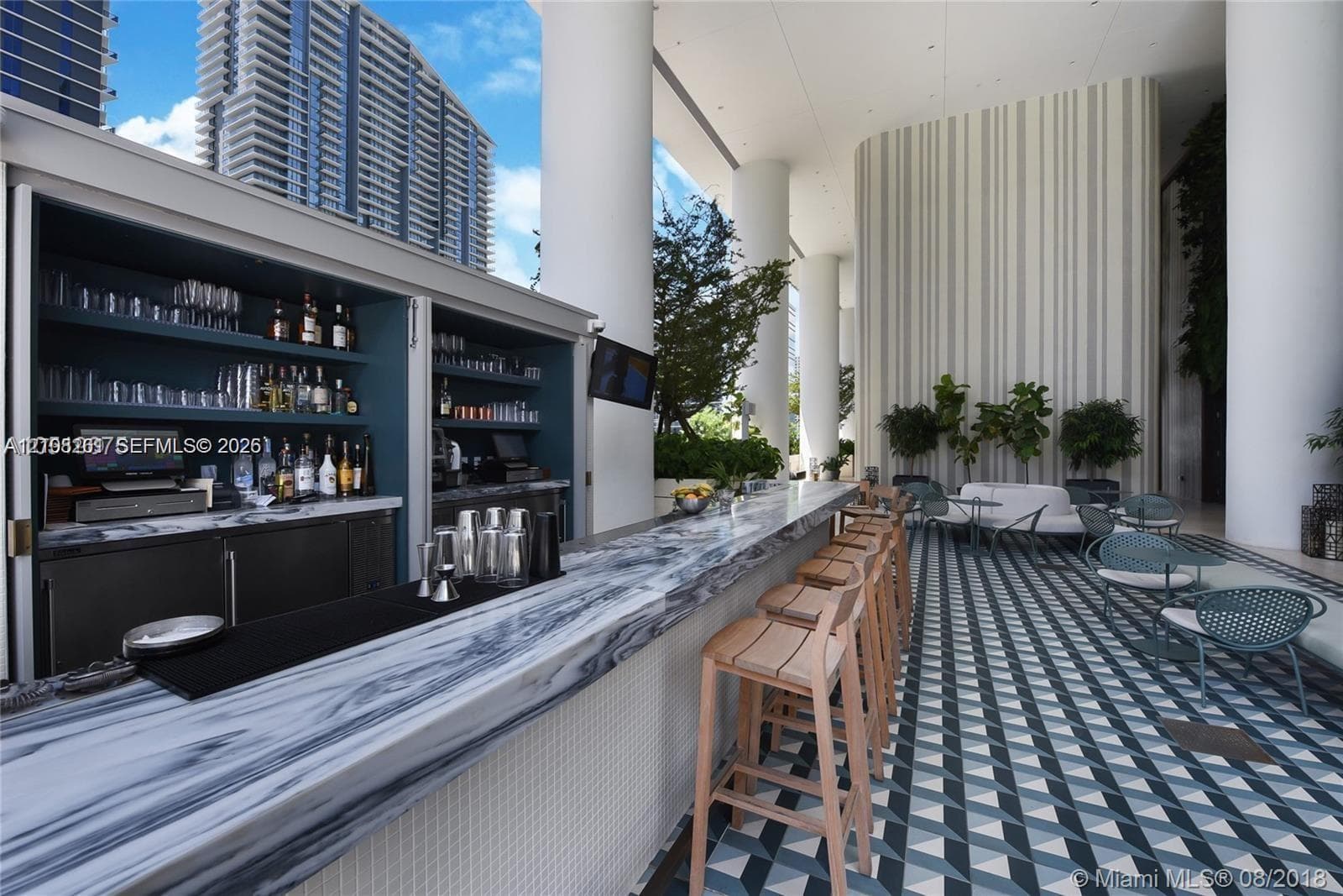 Outdoor bar featuring a stone-surface countertop, built-in shelving, geometric patterned tile flooring, and oversized structural columns