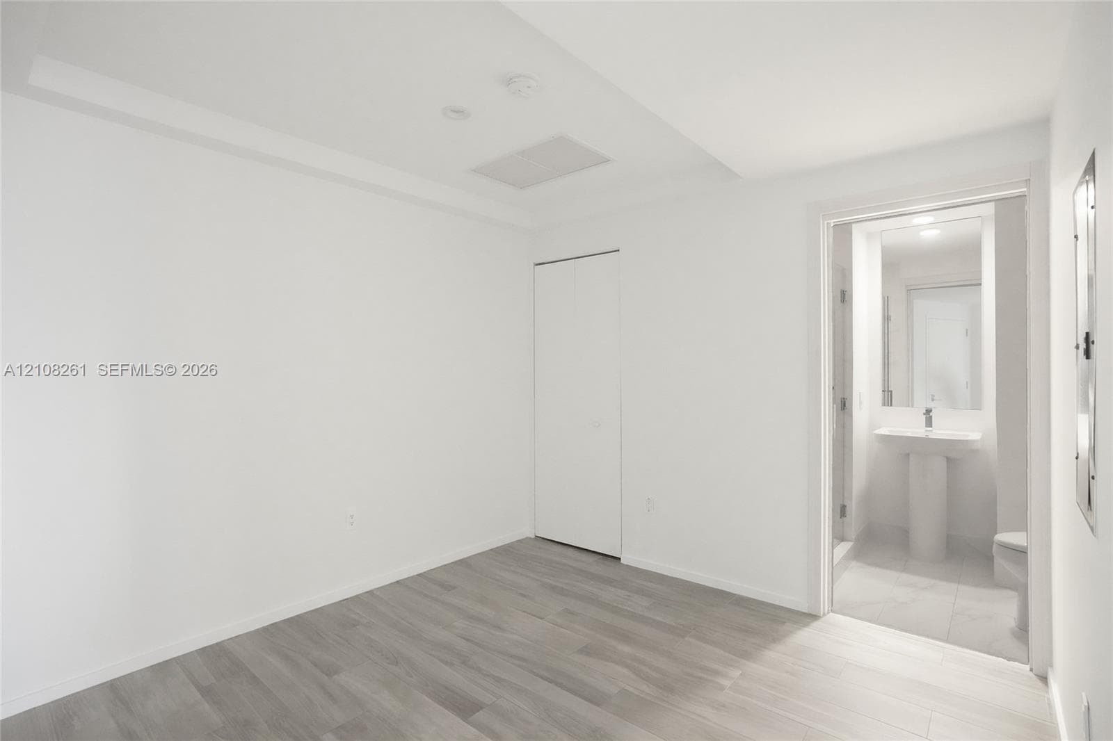 Room featuring neutral-toned wood-finish flooring, a bi-fold closet, and entry to a tiled bathroom equipped with a pedestal sink
