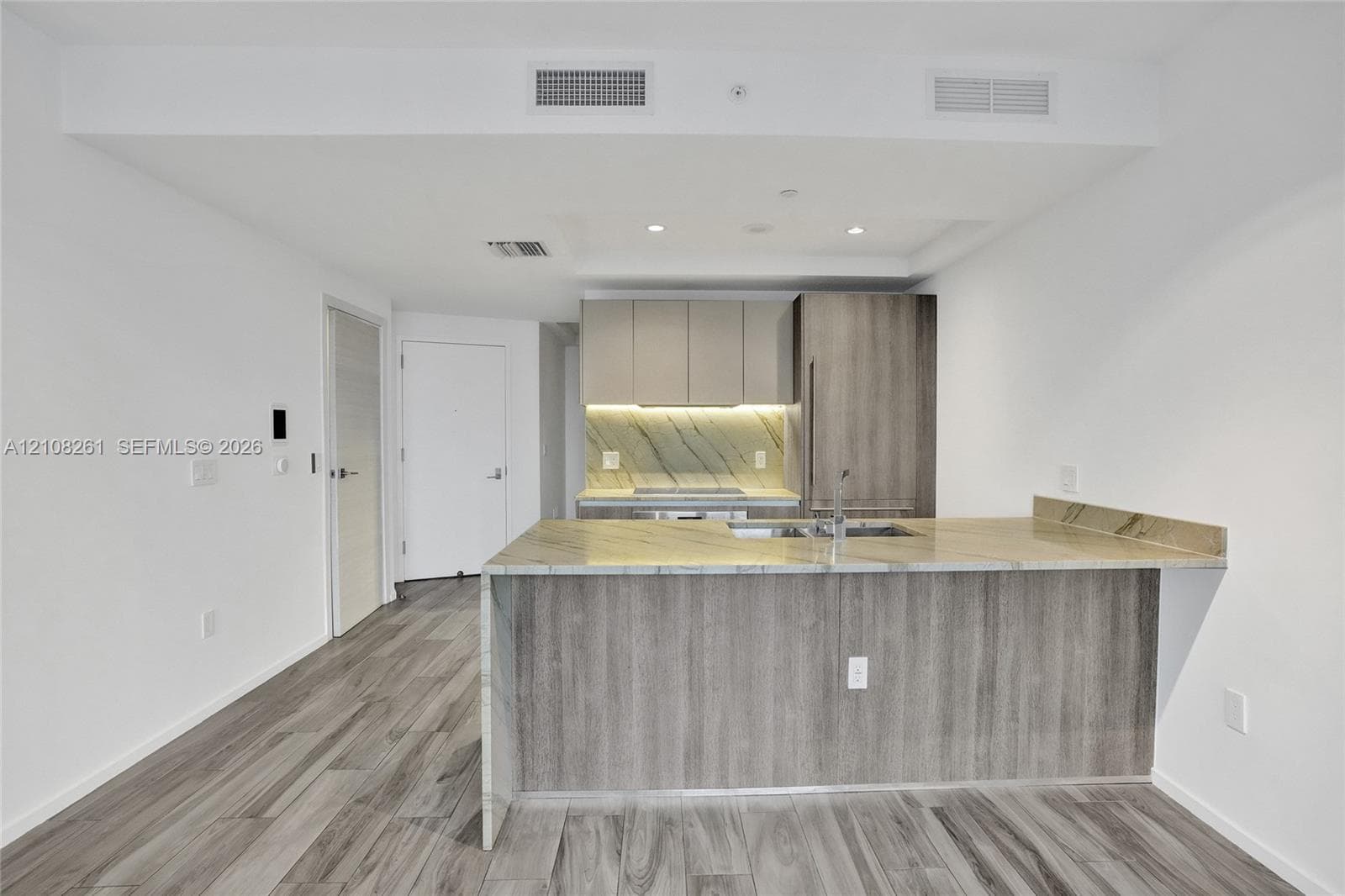Kitchen featuring an island with a stone countertop, wood-finish cabinetry, built-in panel-ready refrigerator, integrated cooktop, and wood-finish flooring