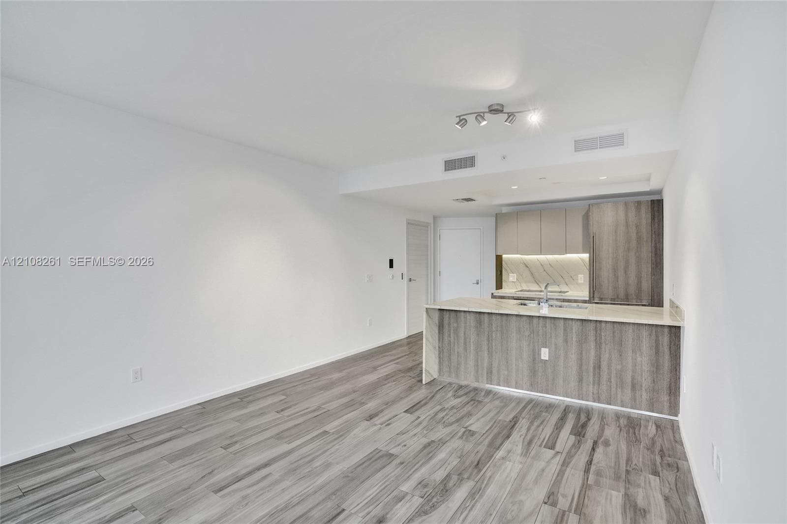Open-concept area featuring wood-finish flooring, kitchen cabinetry with a wood-grain aesthetic, stone-finish countertops, and a full-height stone-finish backsplash