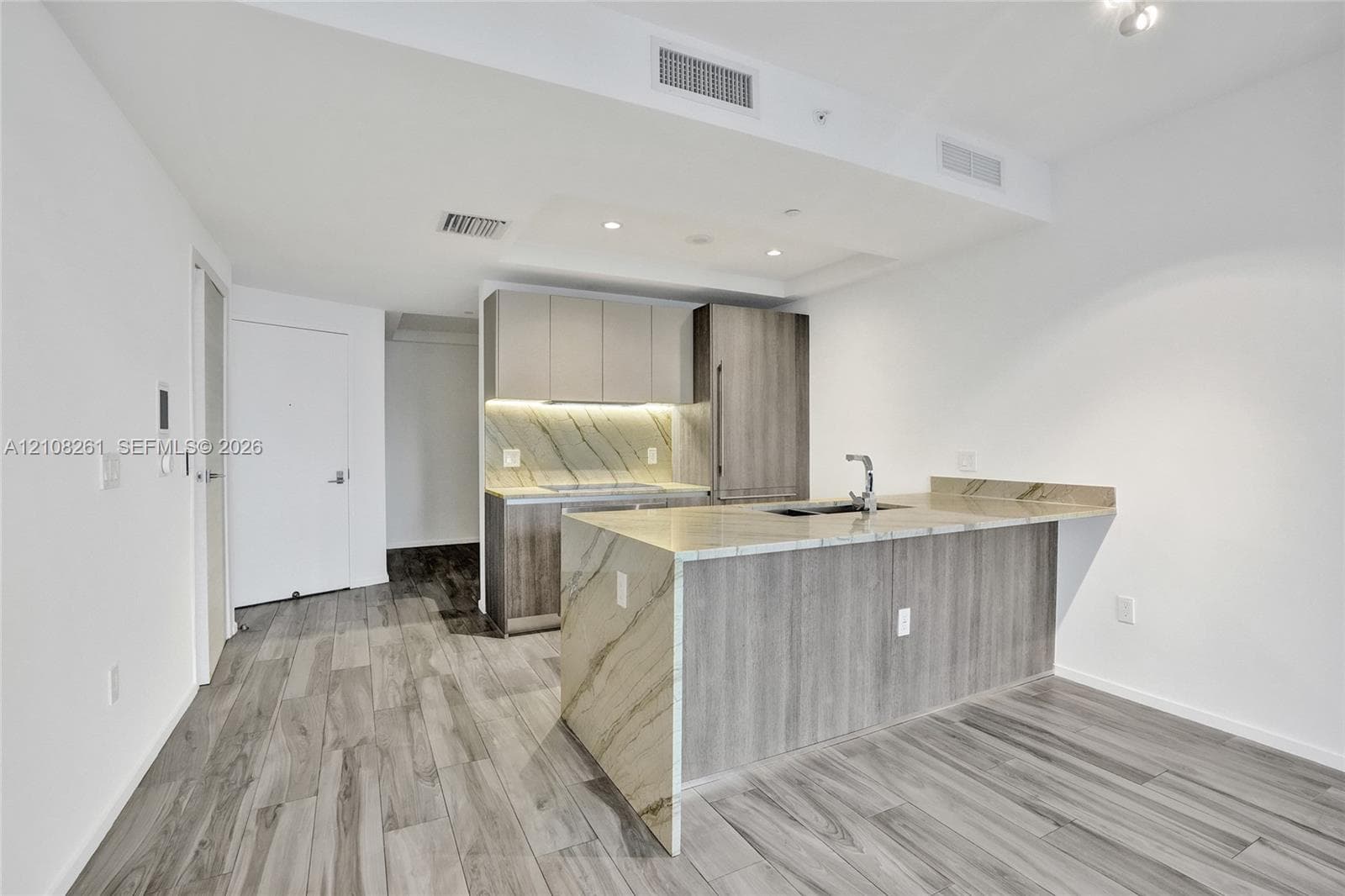 Kitchen featuring flat-panel cabinetry, stone-surface waterfall island, integrated refrigerator, recessed lighting, and wood-finish flooring