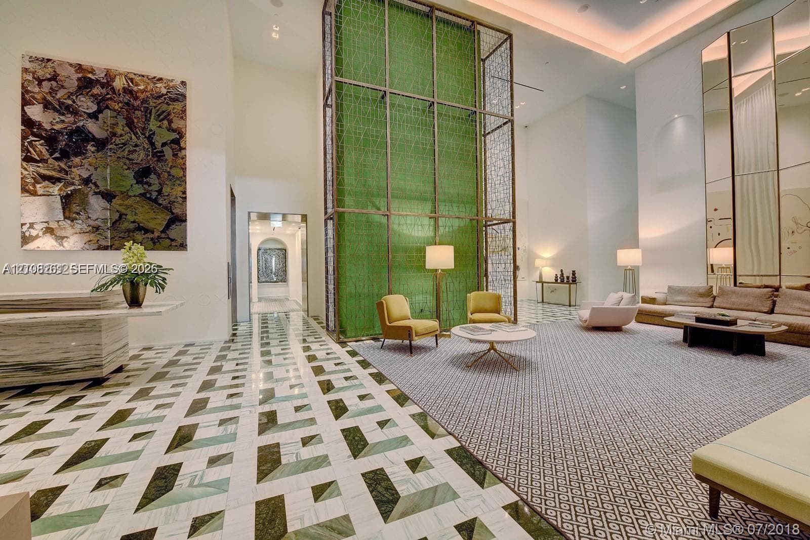 Double-height foyer featuring geometric stone flooring, a soaring floor-to-ceiling metal architectural screen, recessed cove lighting, and full-length mirrored wall panels