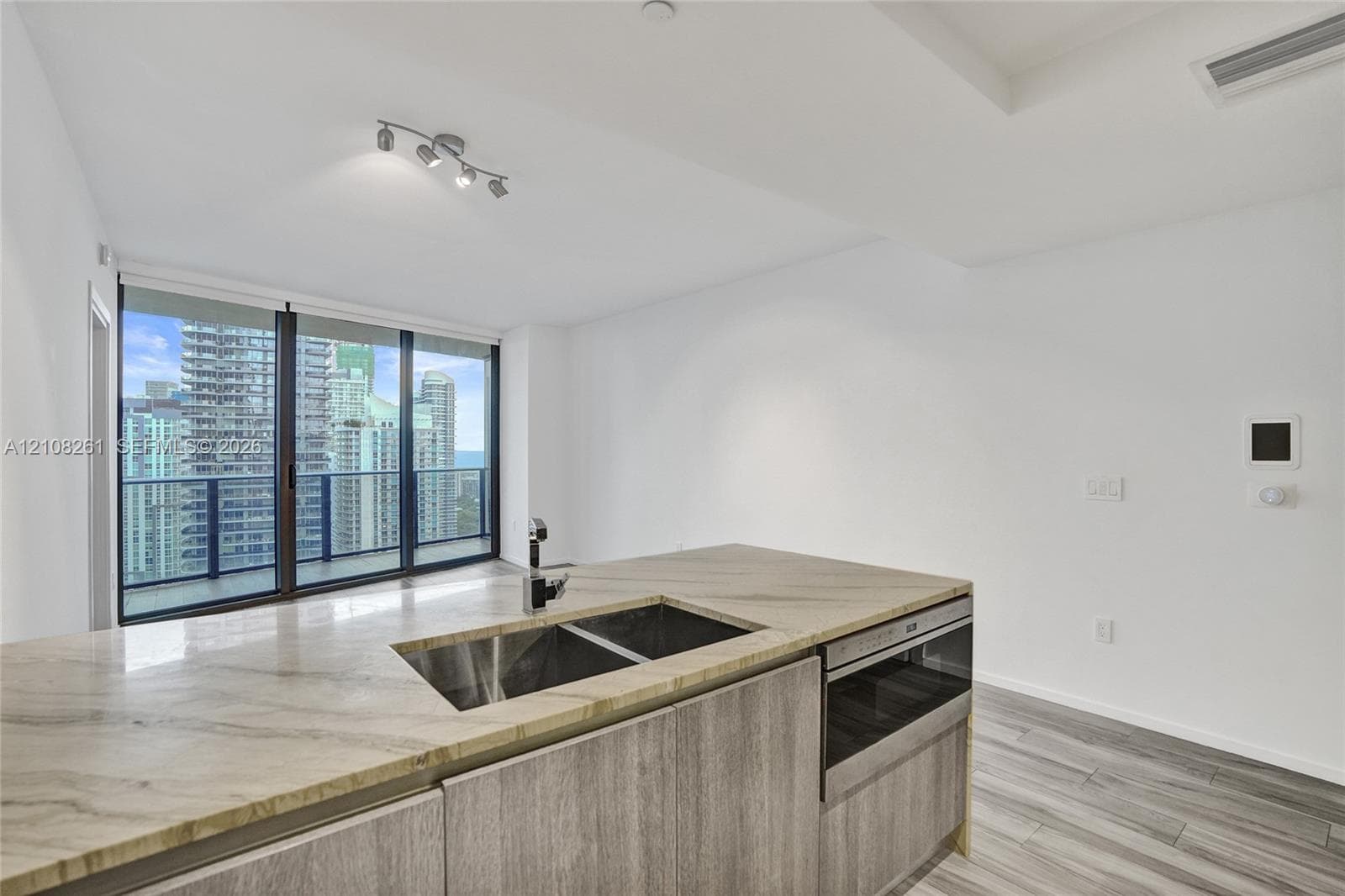 Kitchen island featuring stone countertops, integrated stainless steel sink, wood-finish cabinetry, built-in microwave, and wood-finish flooring