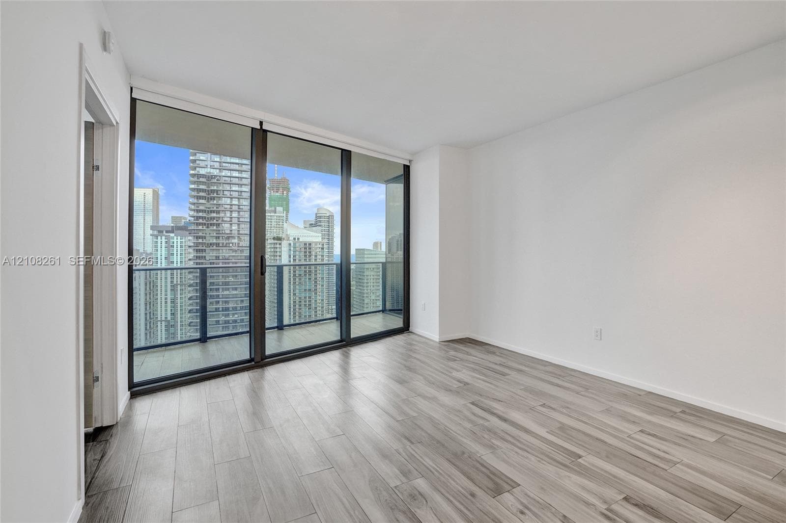Floor-to-ceiling windows, wood-finish flooring, and an attached balcony with dark metal railings