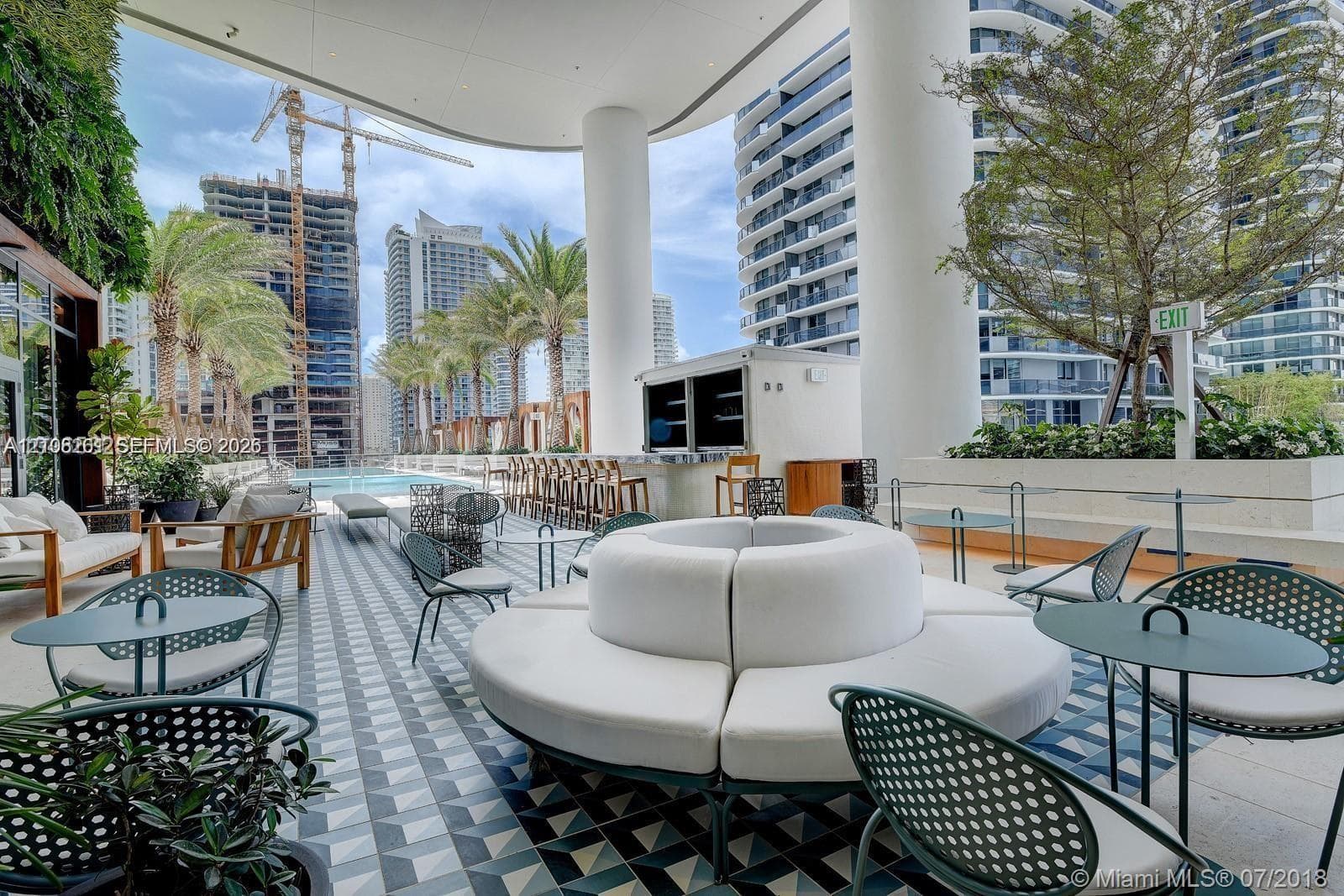 Covered terrace featuring geometric patterned floor tiling, built-in outdoor bar with countertop, recessed lighting, and integrated landscaping