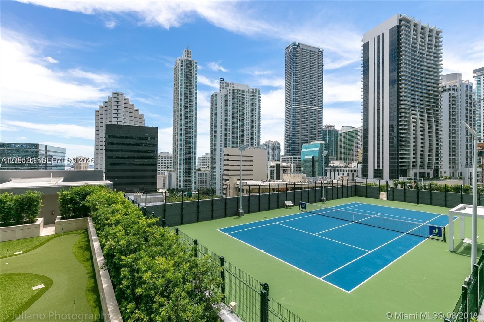 Rooftop recreational level featuring a hard-court tennis surface and synthetic putting green with perimeter fencing
